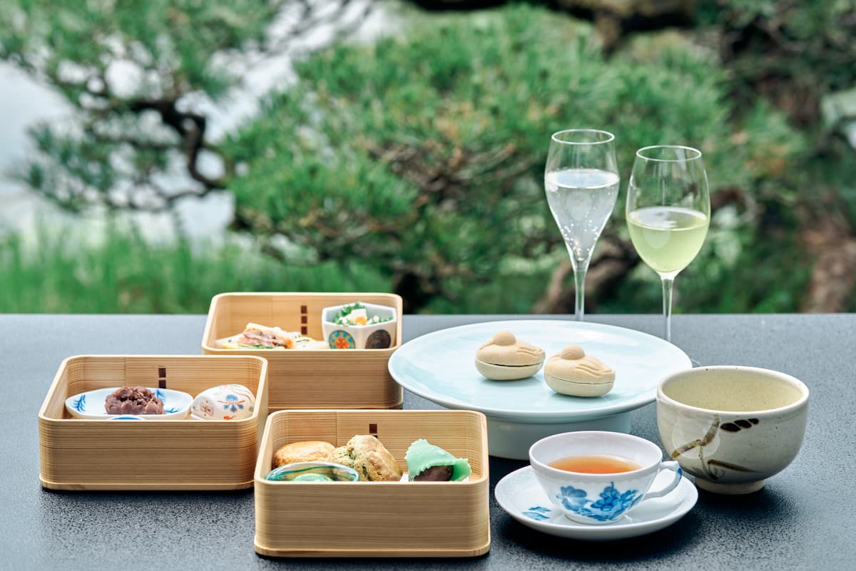 Afternoon tea and tiered bento boxes with sparkling wine served outdoors beside the manicured pine garden at Ohana