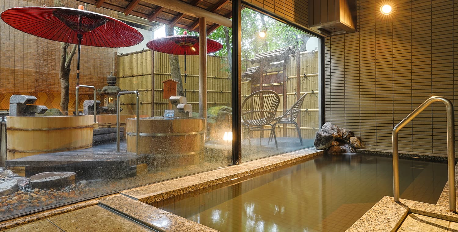 Open-air onsen bath at Ryokufukaku with red Japanese umbrellas and bamboo fence