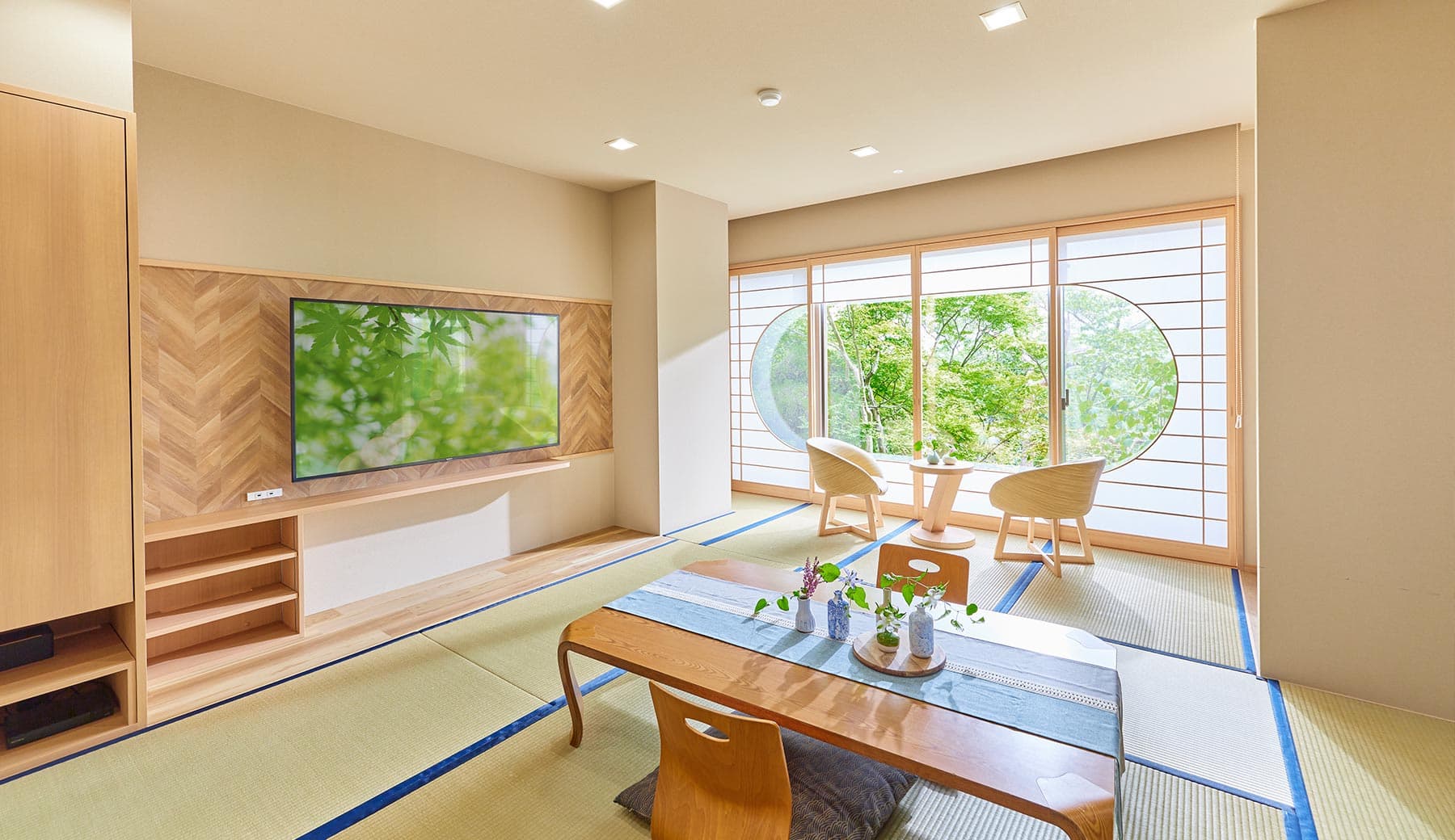 Modern Japanese-style guest room with tatami flooring, low dining table and a round picture window framing green maples at Motoyu Ryusenkaku, Arima Onsen