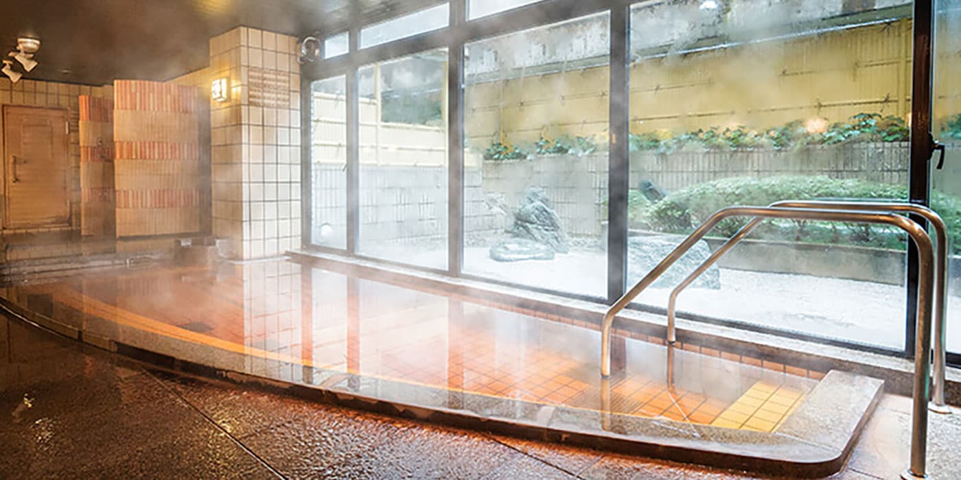 Steamy indoor hot-spring bath with tiled tub and garden view at Kanazawa Hakuchoro Hotel Sanraku