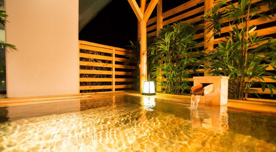 Open-air hinoki bath lit at night beside the river