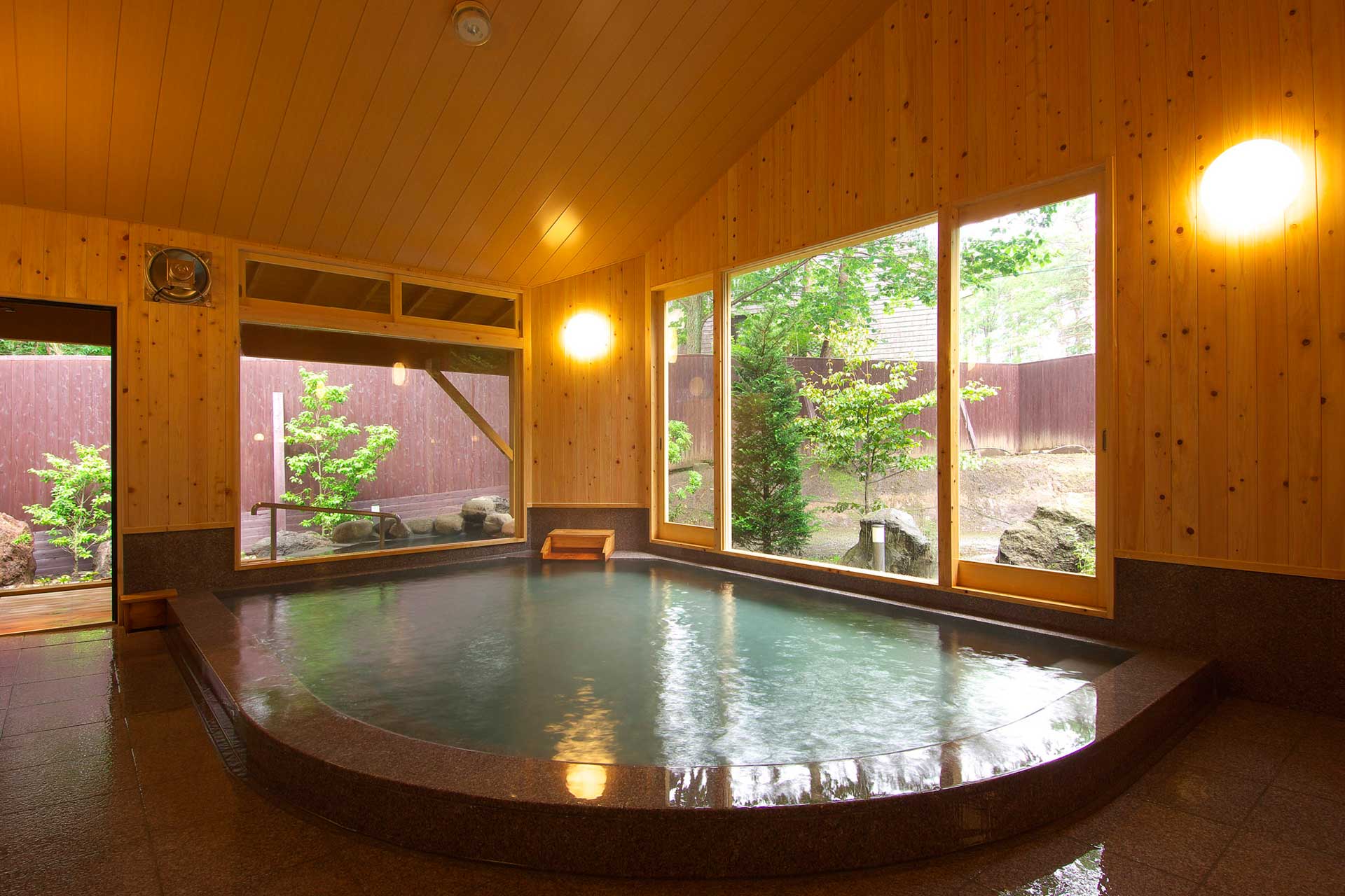 Indoor wooden hot spring bath at Kusatsu Skyland Hotel with a vaulted cedar ceiling and a window onto the garden