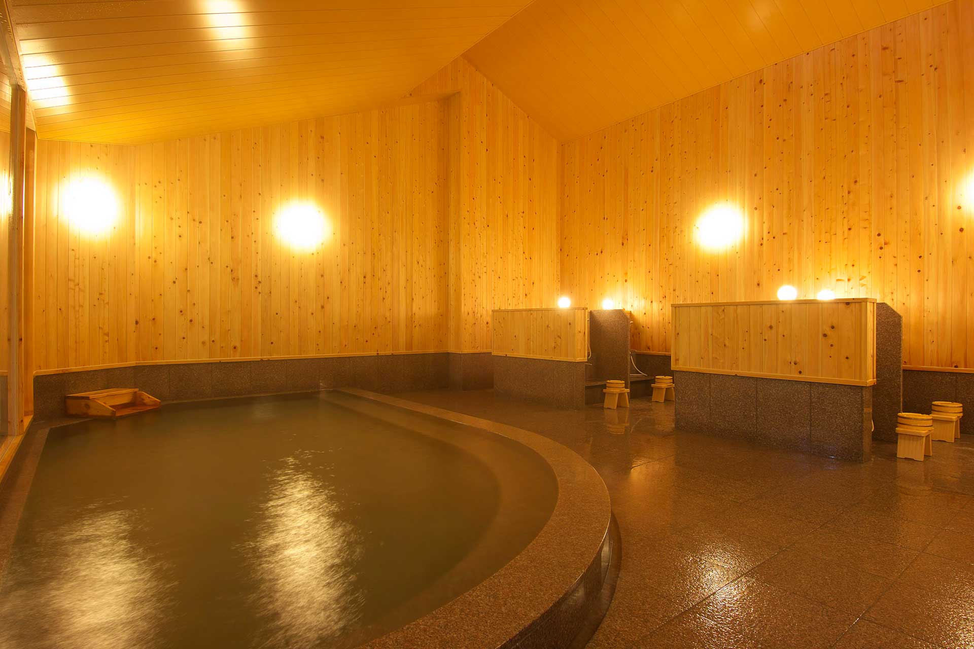 Spacious indoor cypress-lined hot spring bath at Kusatsu Skyland Hotel with warm lighting and stone flooring
