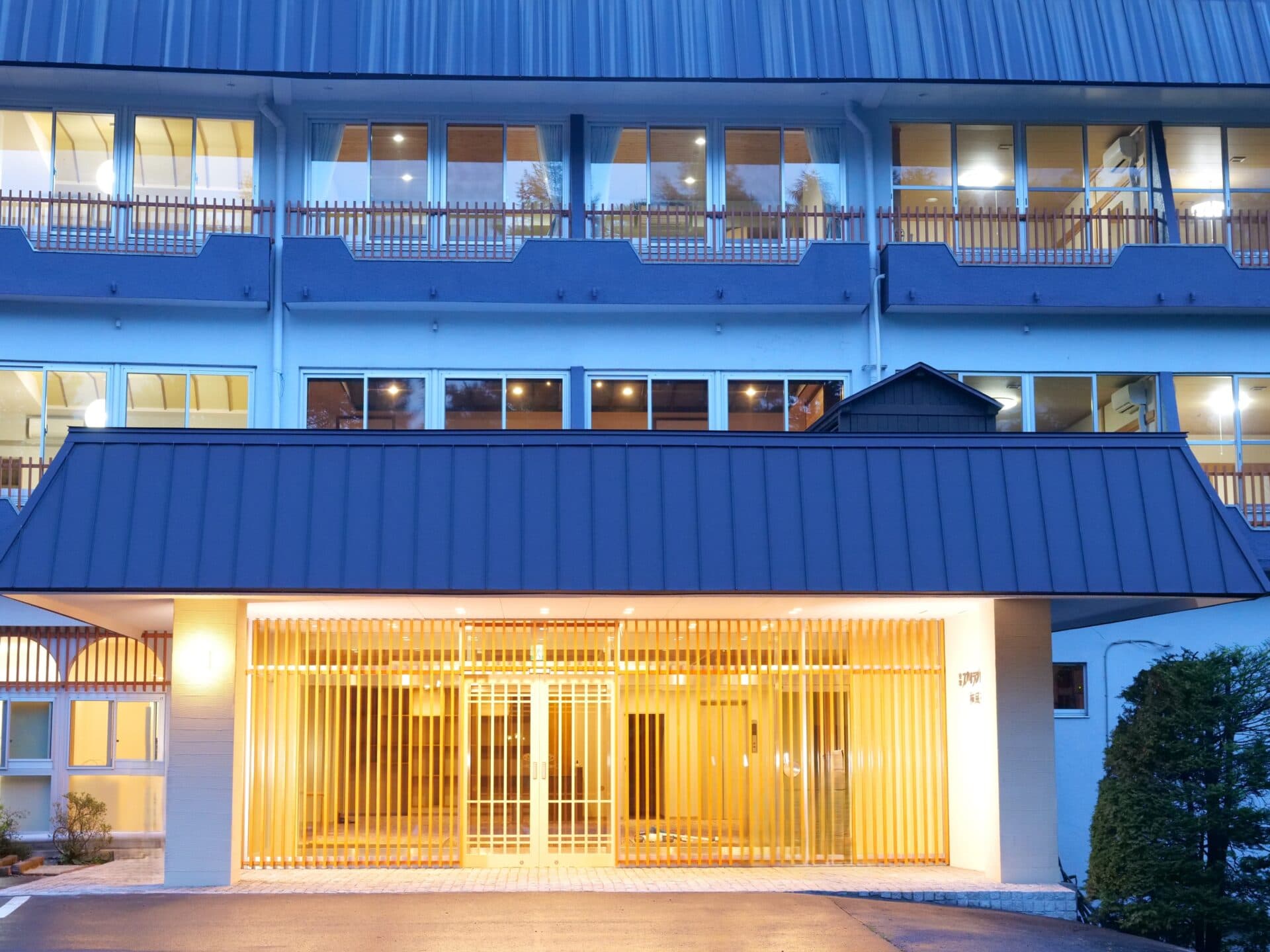 Illuminated entrance and facade of Kusatsu Skyland Hotel Seifutei at dusk with a tile-roofed porch and lattice doors