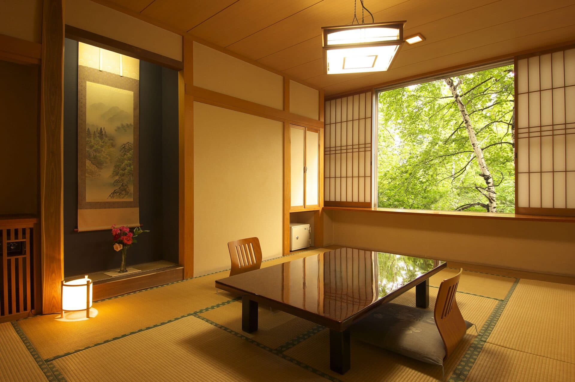 Japanese-style tatami guest room at Kusatsu Skyland Hotel with a hanging scroll in the tokonoma alcove and a window framing green foliage