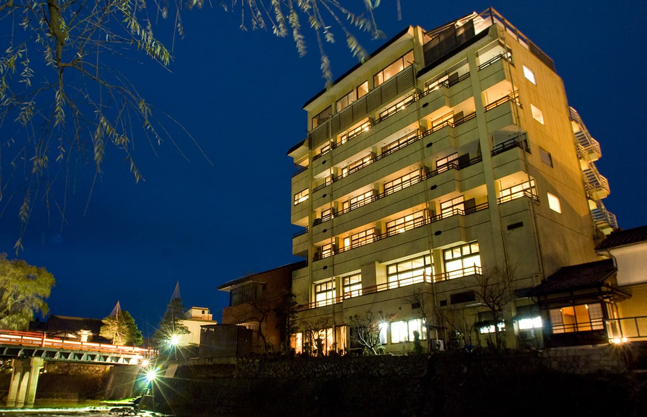 Honjin Hiranoya Kofukan multi-story ryokan lit at dusk beside the Enako River in Takayama Onsen