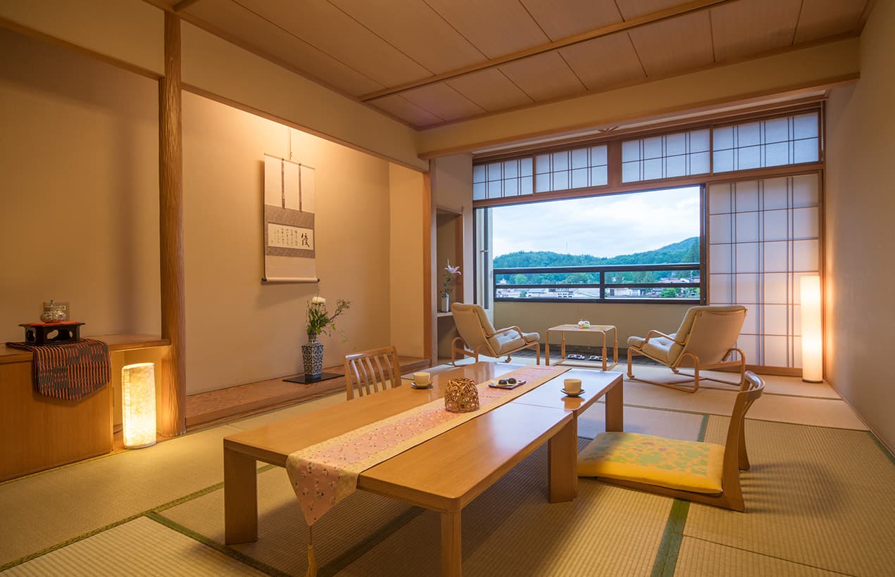 Tatami guest room at Honjin Hiranoya Kofukan with low table, lounge chairs and a Takayama townscape view through shoji windows