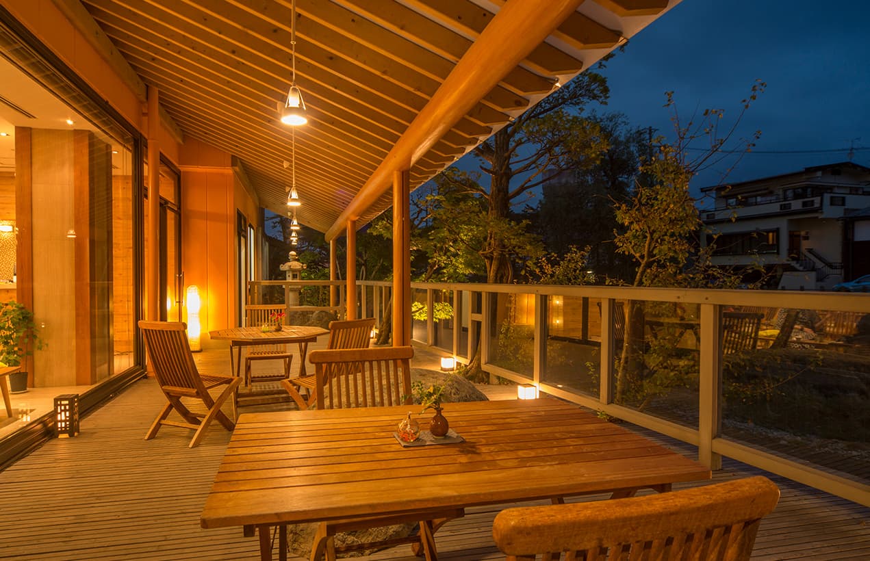 Covered wooden terrace lounge with deck chairs and lanterns overlooking the garden at dusk at Honjin Hiranoya Kofukan
