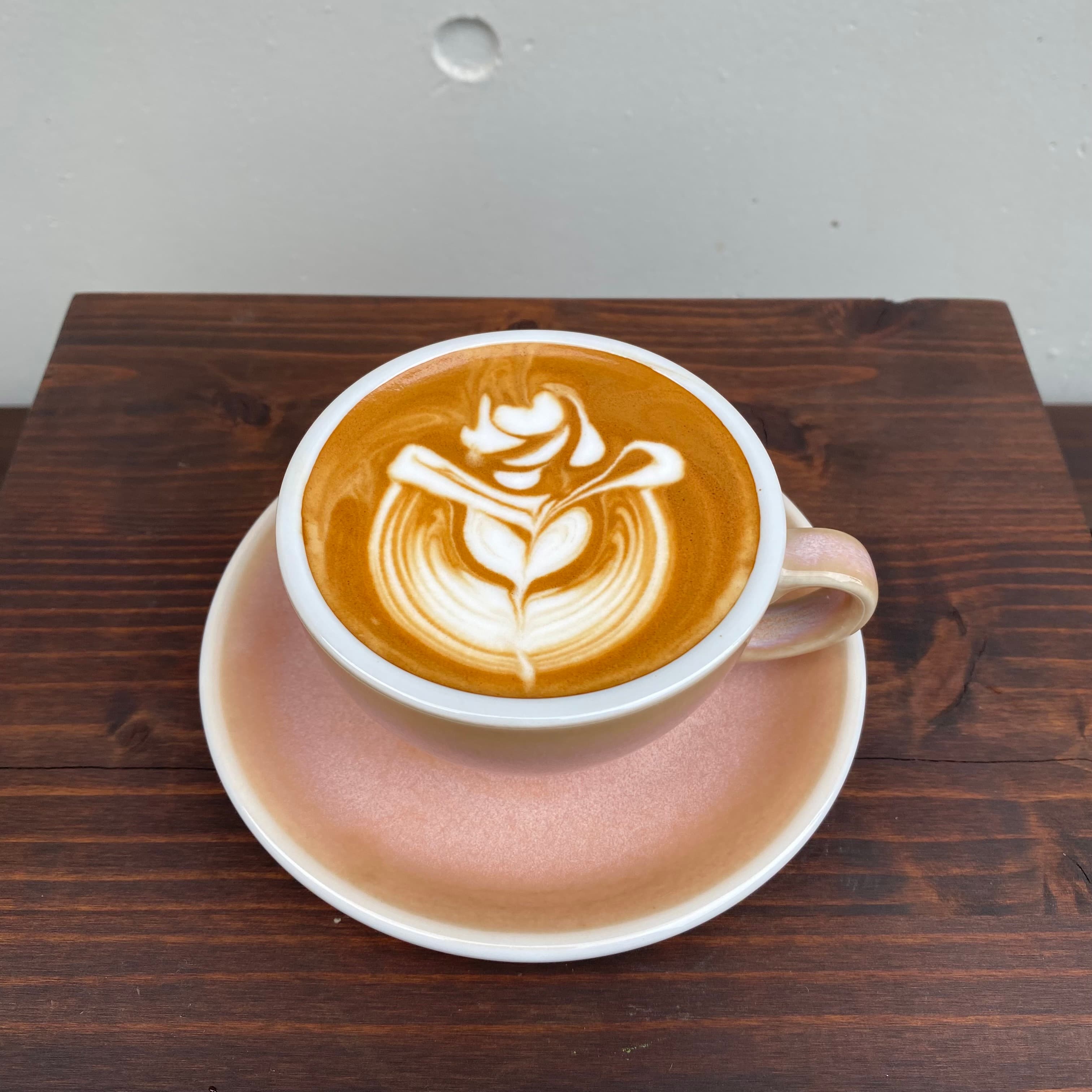 Latte with rosetta art in a pink cup on a wooden table at the Kimi Ryokan cafe in Ikebukuro Tokyo