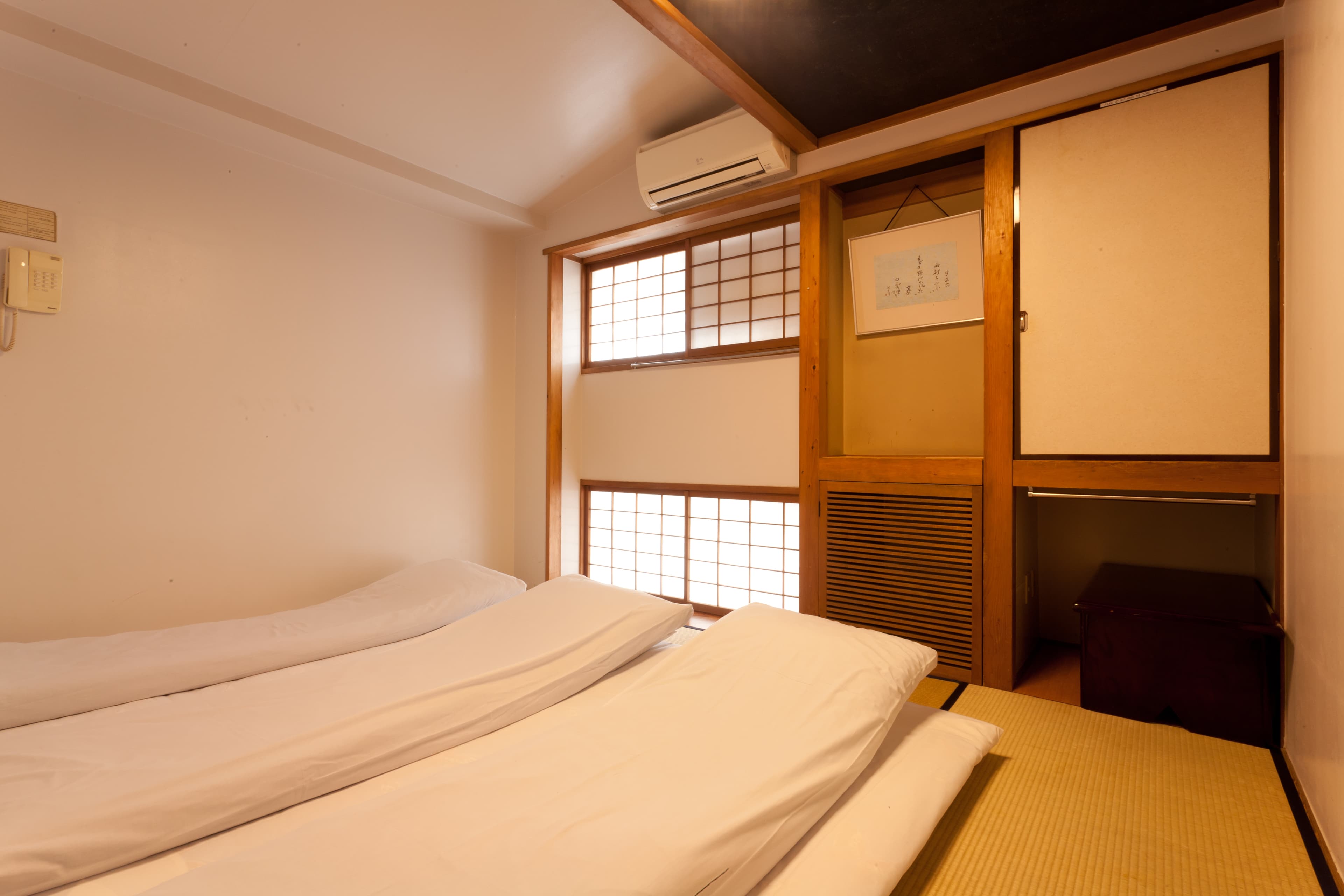 Twin-futon tatami room at Kimi Ryokan Tokyo with wood-framed shoji windows and calligraphy scroll