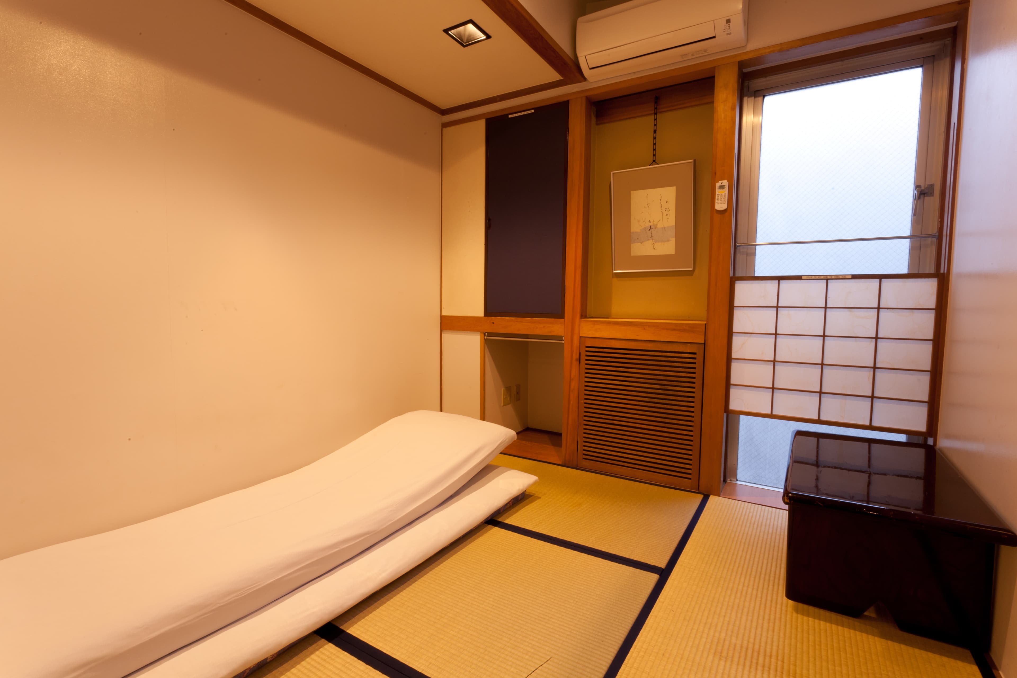 Compact Japanese tatami room at Kimi Ryokan Ikebukuro with a single futon, scroll and shoji window