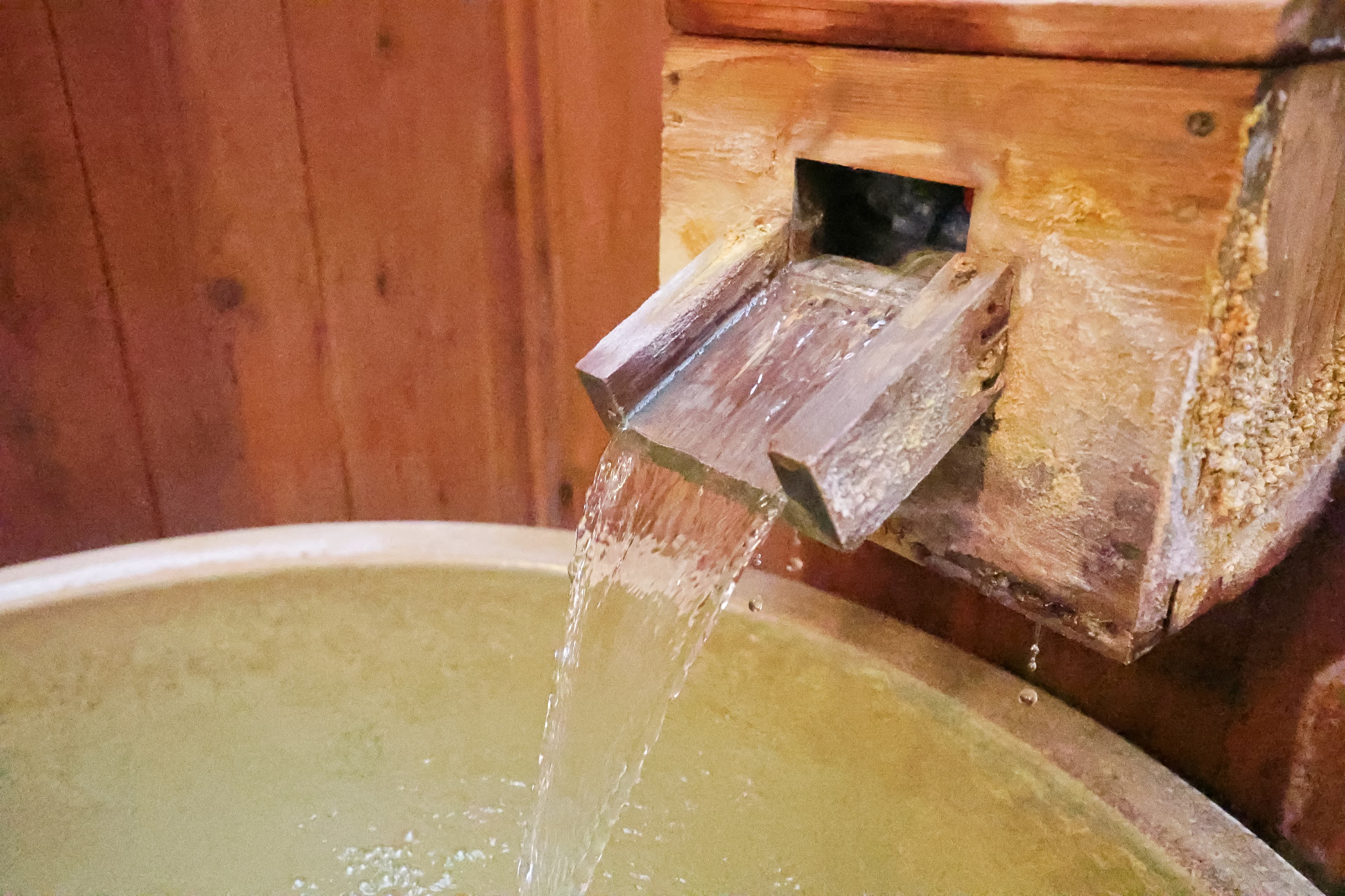 Close-up of a wooden spout pouring sulfur thermal water into a stone bath