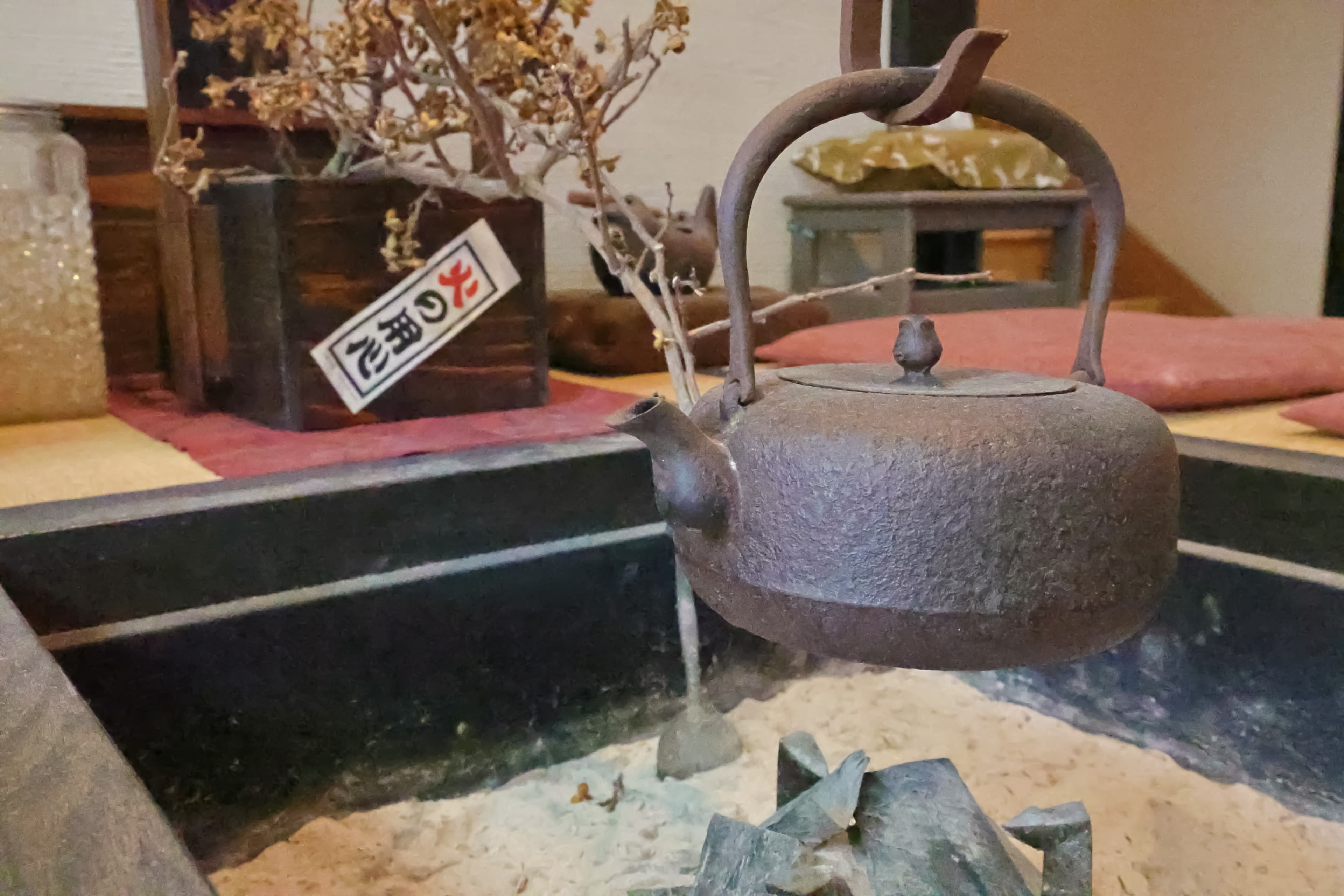 Cast-iron kettle hanging over a charcoal irori hearth with a dried-flower arrangement behind