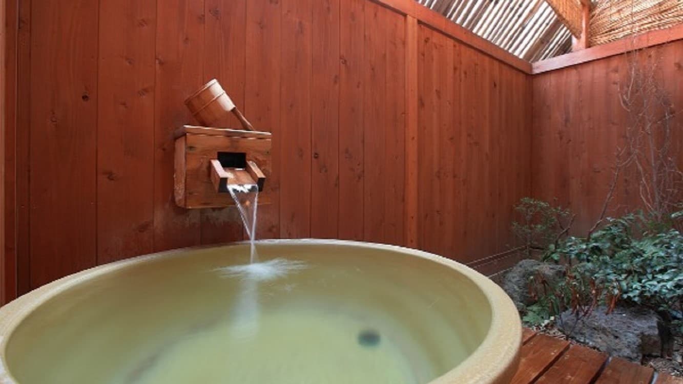 Private open-air round wooden tub on a balcony filled with greenish Yubatake-source water