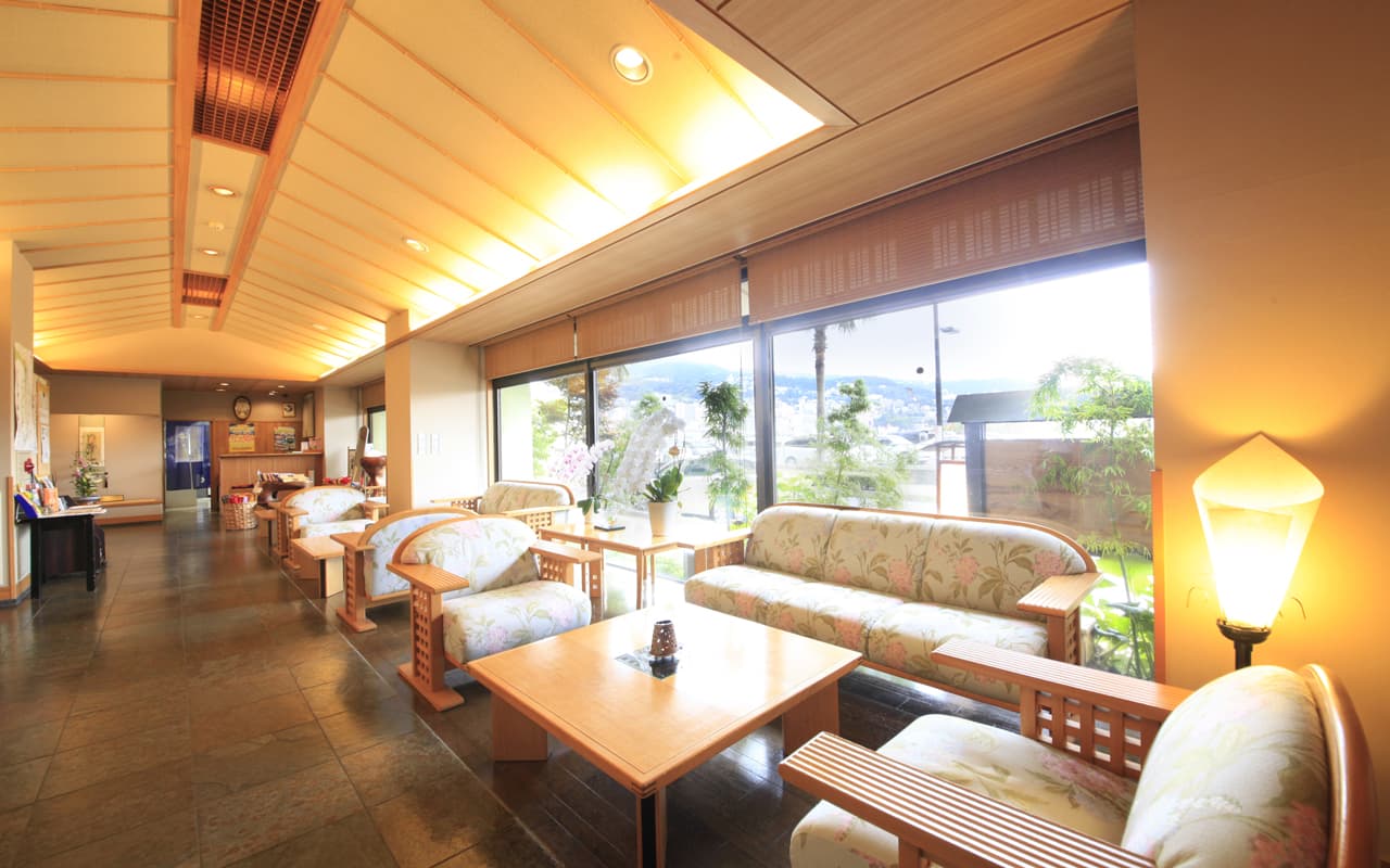 Lobby lounge with rattan seating and floor-to-ceiling windows overlooking Atami town and sea
