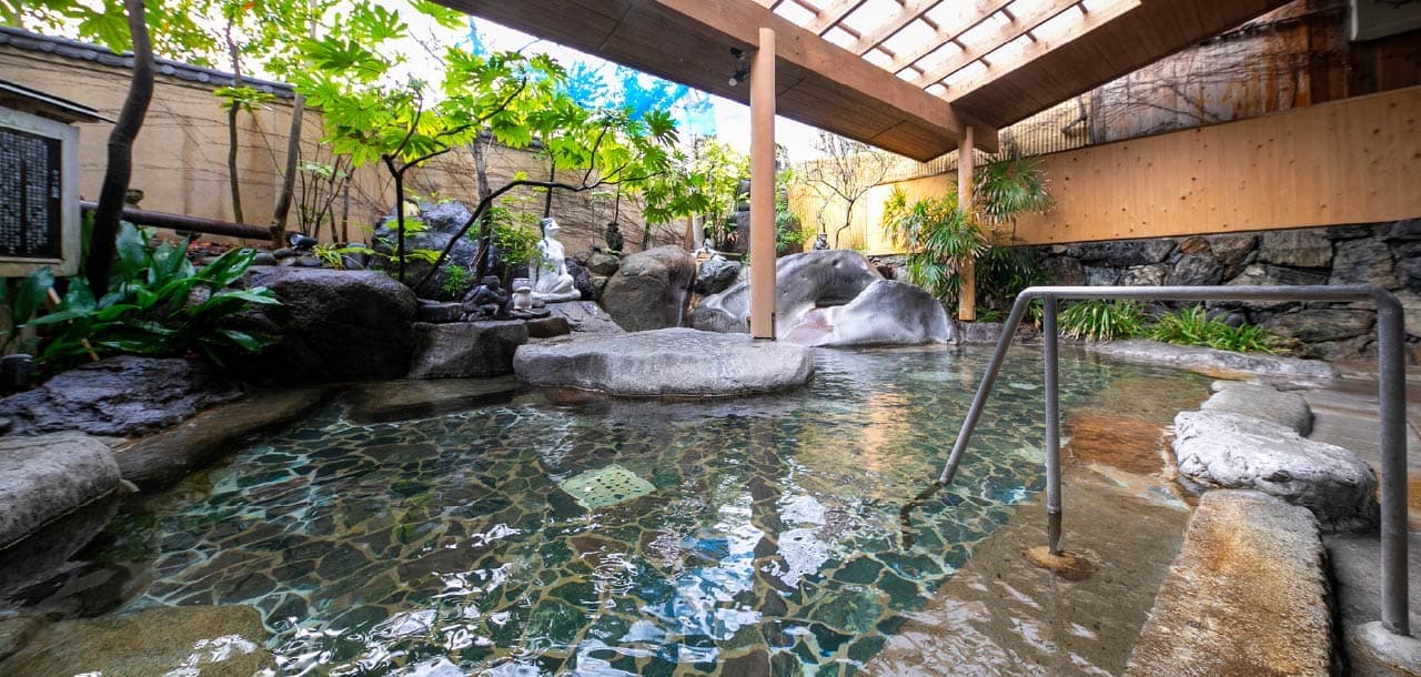 Rock-framed outdoor onsen bath at Taisenkaku surrounded by greenery and a small stone statue