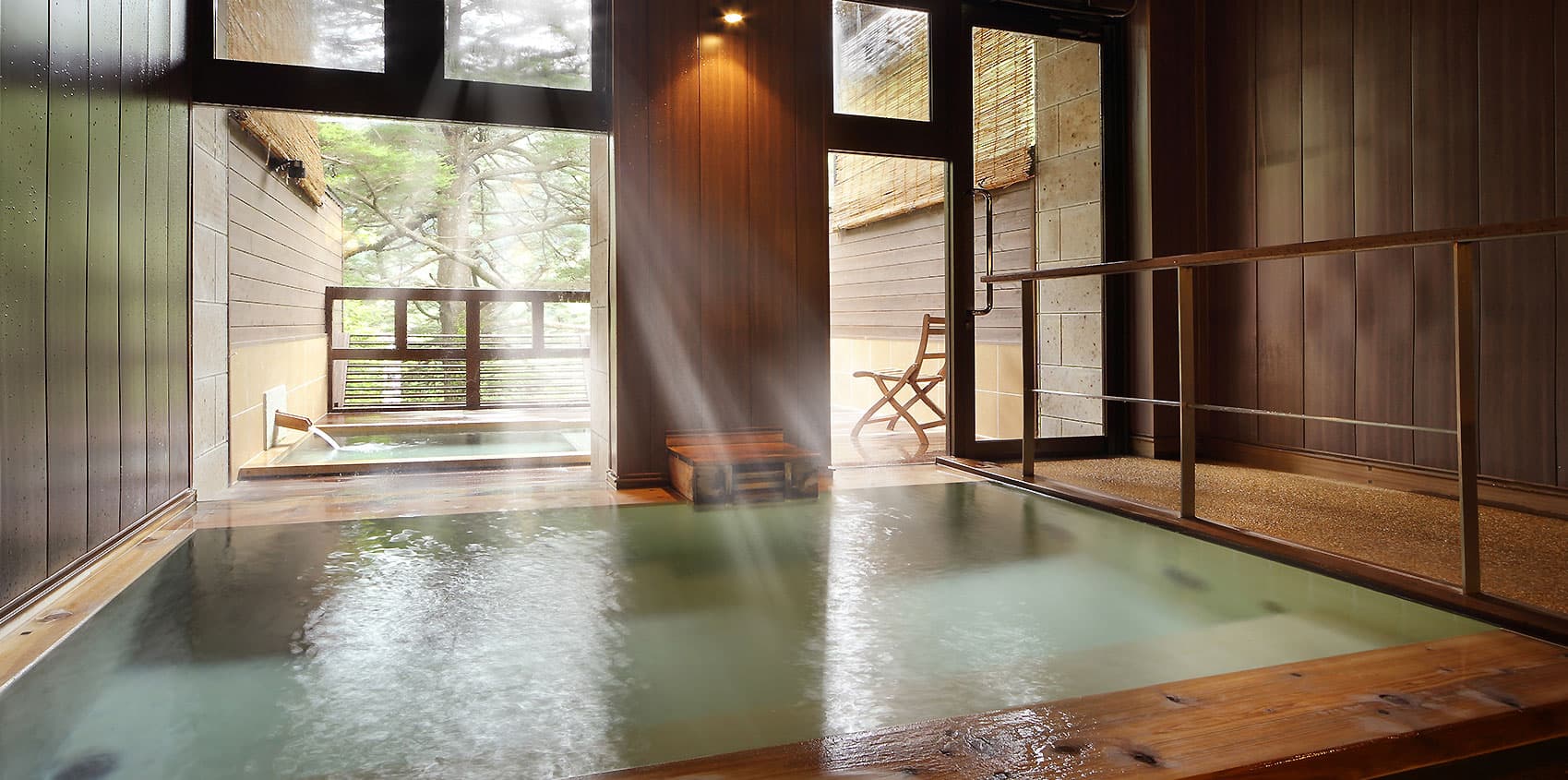 Indoor hot-spring bath at Hotel Tsuga no Ki with rising steam and light streaming through tall windows onto the forest