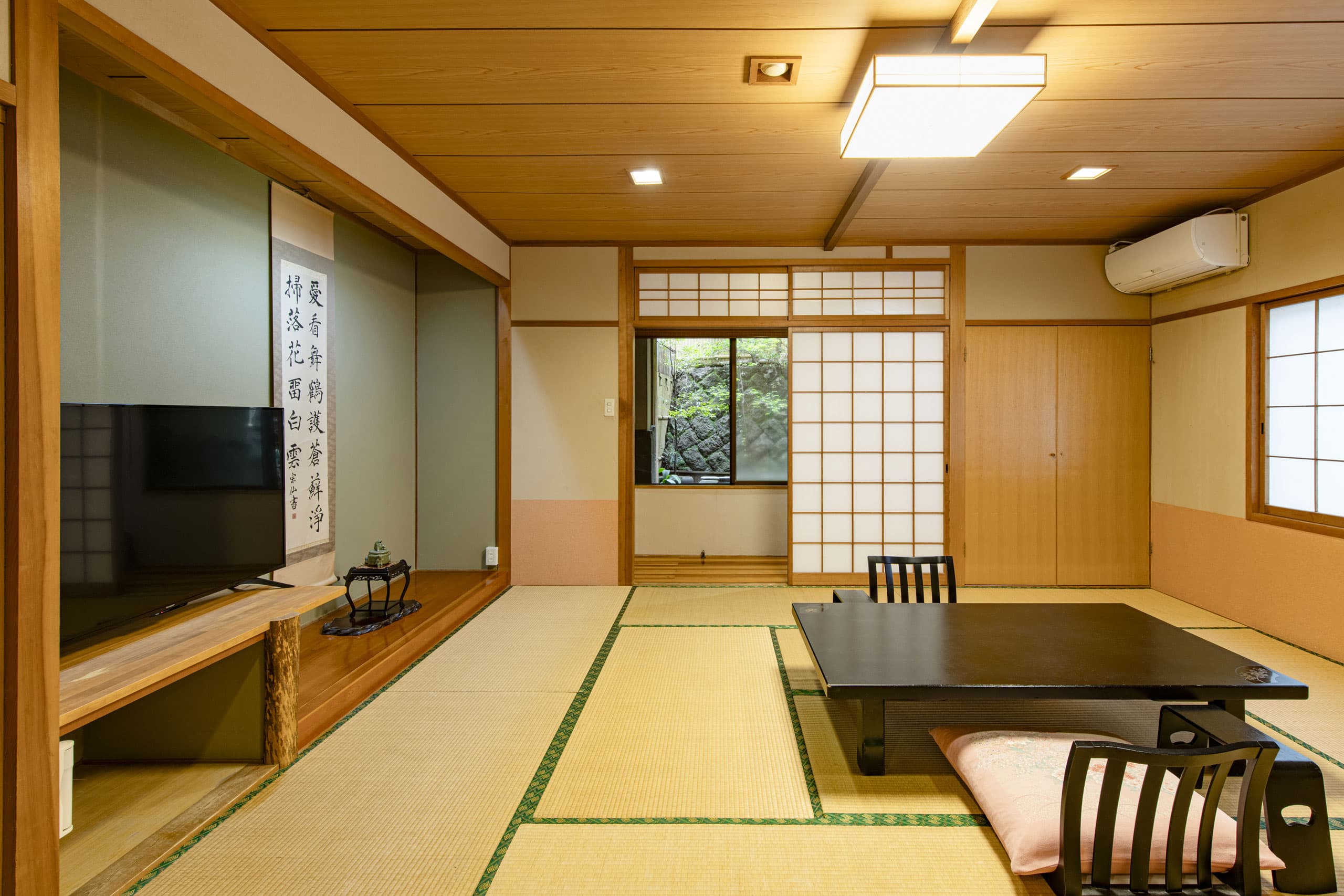 Japanese-style tatami guest room with low table, hanging scroll and garden-view window at Unzen Iwaki Ryokan