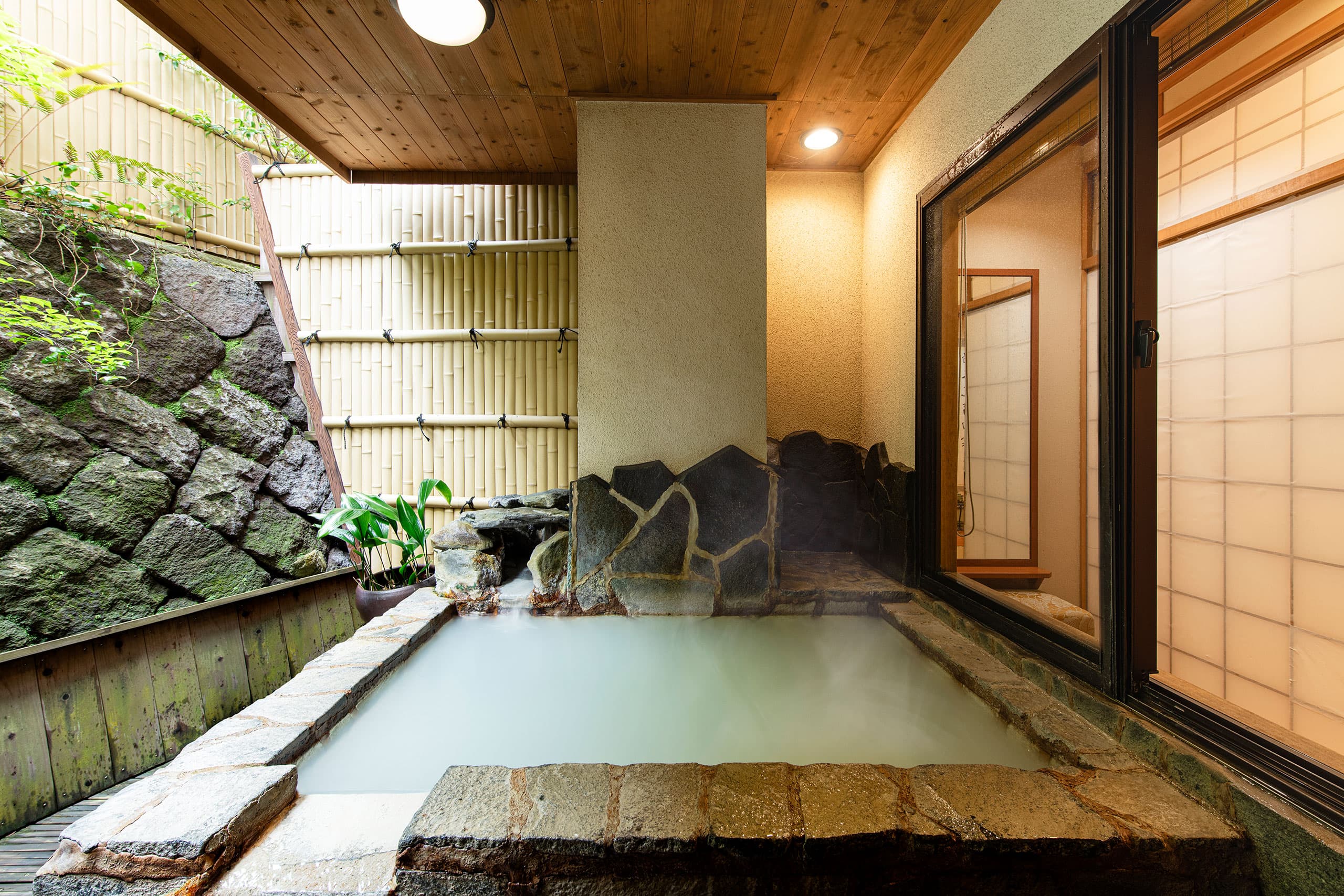 Private indoor stone bath with milky Unzen hot spring water beside a shoji screen window at Unzen Iwaki Ryokan