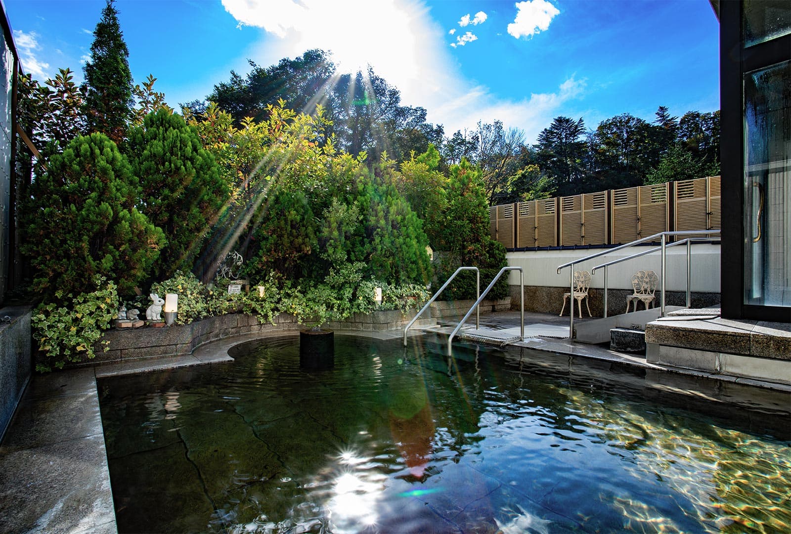 Rantei outdoor rotenburo garden open-air bath with emerald mineral water surrounded by maples and bamboo fence under blue sky