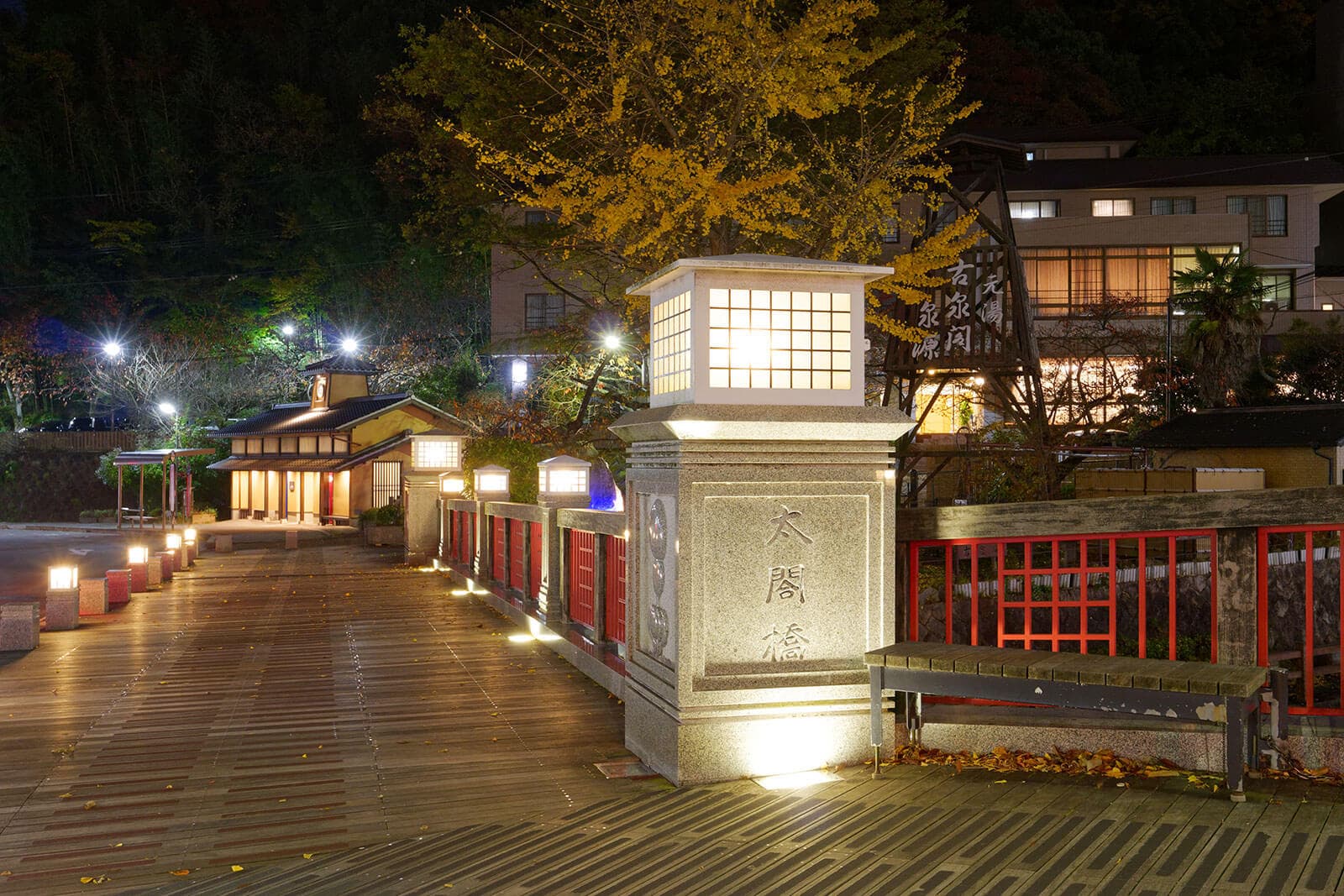 Arima Onsen townscape at night near Arima Gyoen with the Taikobashi bridge railings, stone lantern and a glowing golden ginkgo tree