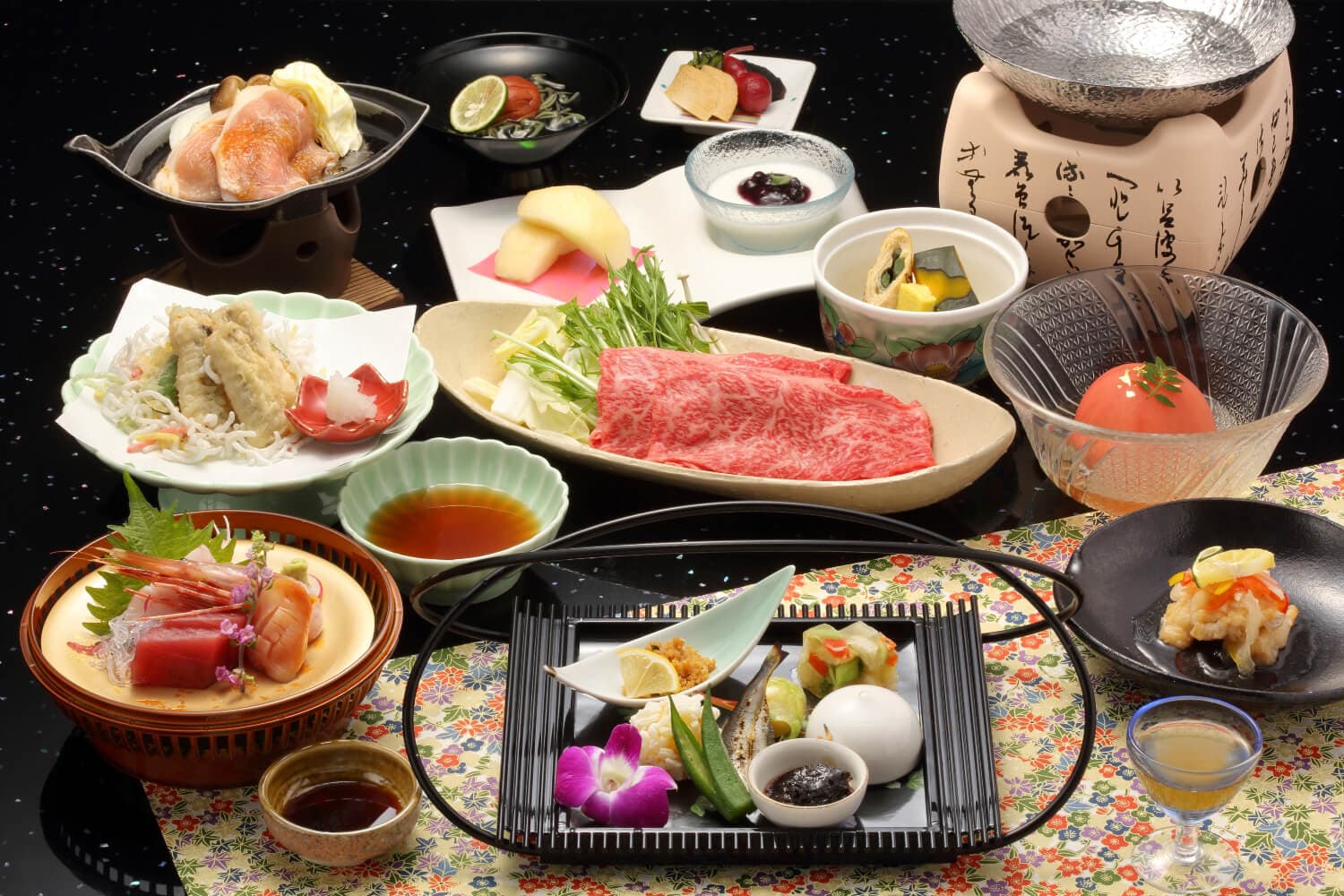 Multi-course kaiseki dinner at Arima Gyoen centered on a platter of marbled Kobe beef for hot pot, with sashimi, tempura, simmered vegetables and assorted small dishes on a black table