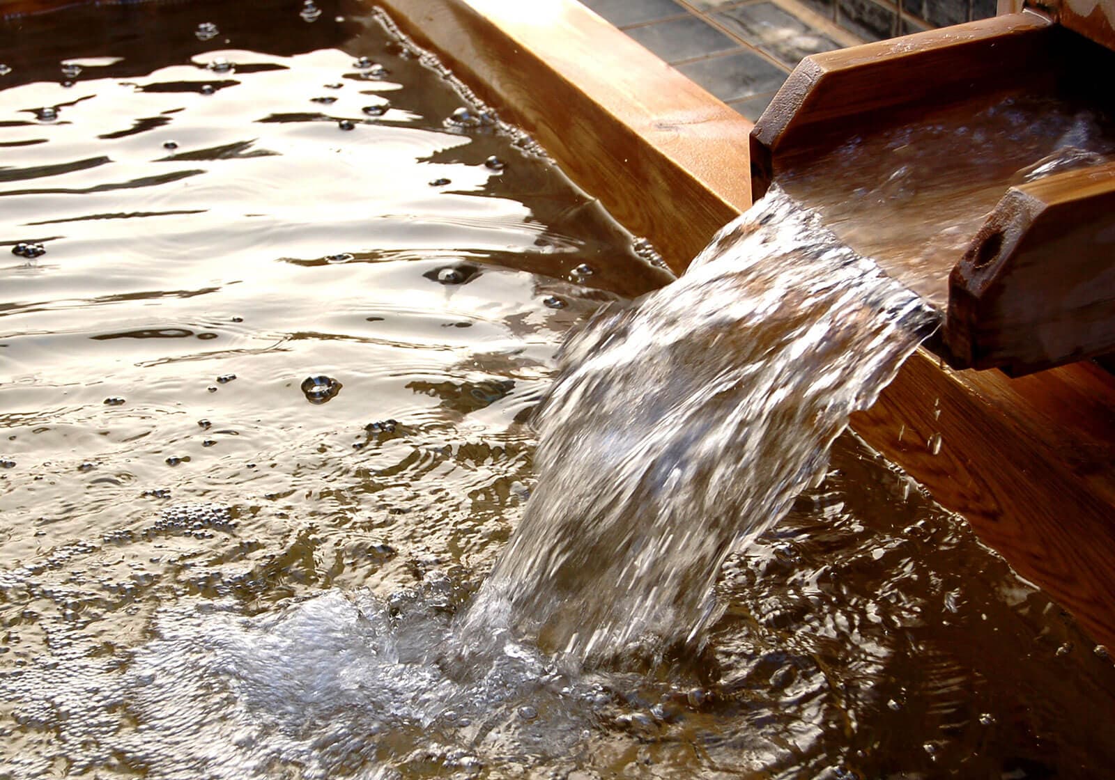 Close-up of golden iron-rich Arima kinsen water pouring from a wooden spout into a bath at Arima Gyoen
