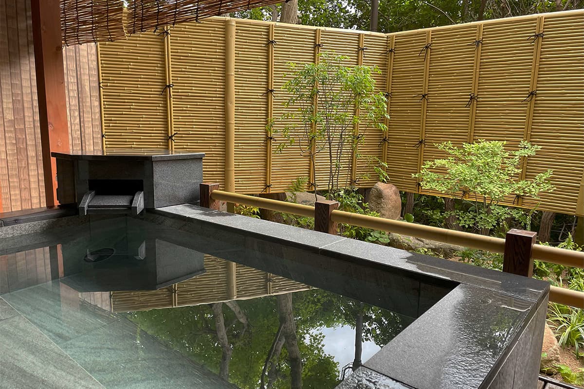 Arima Gyoen open-air bath with polished stone rim and bamboo screen open to a wooded garden