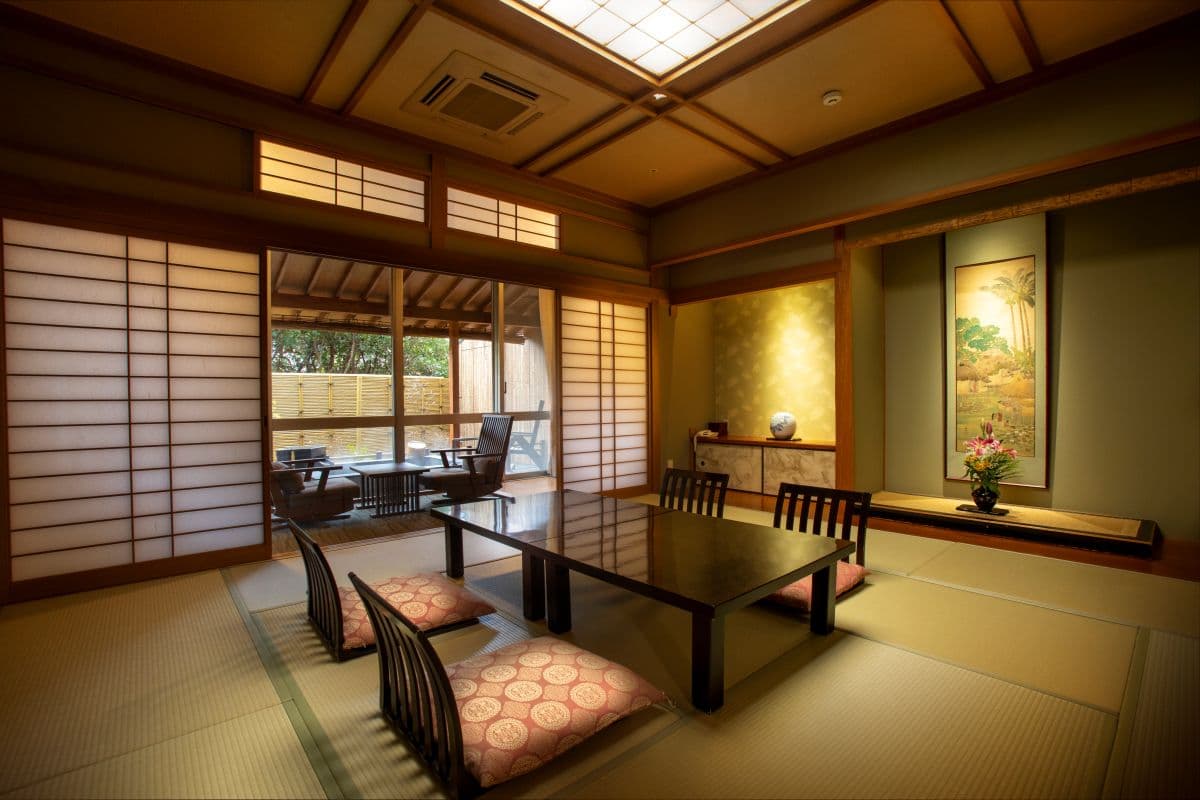 Bright tatami guest room at Arima Gyoen with floor-seating table, hanging scroll and seasonal flower arrangement in the alcove