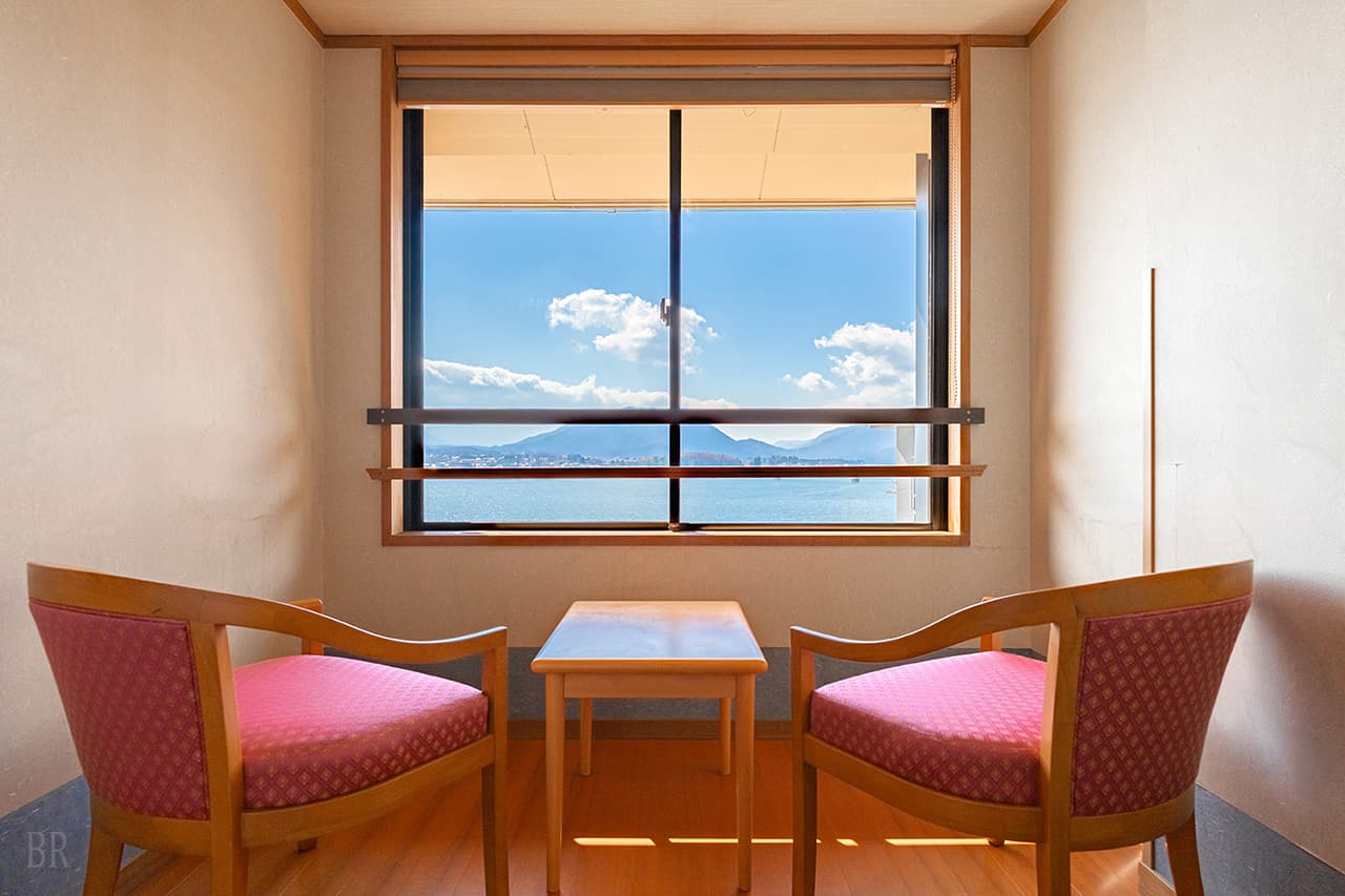 Lake-view guest room at Hotel Asafuji with two armchairs facing a window overlooking Lake Kawaguchi