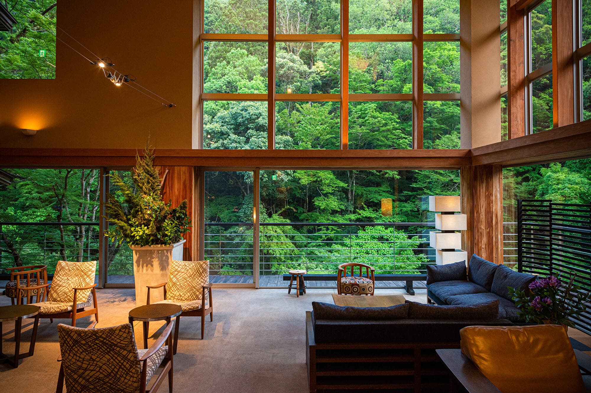 Double-height lounge at Asebino with woven armchairs and floor-to-ceiling windows framing the forest, Yugashima Onsen Izu