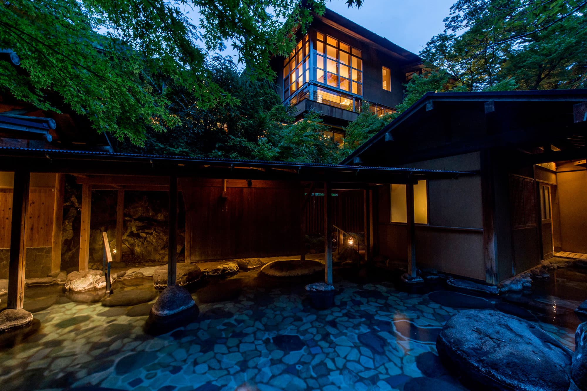 Tanigawa-no-Yu Asebino ryokan exterior at dusk with a lit upper room above a stone-paved open-air bath courtyard, Yugashima Onsen Izu