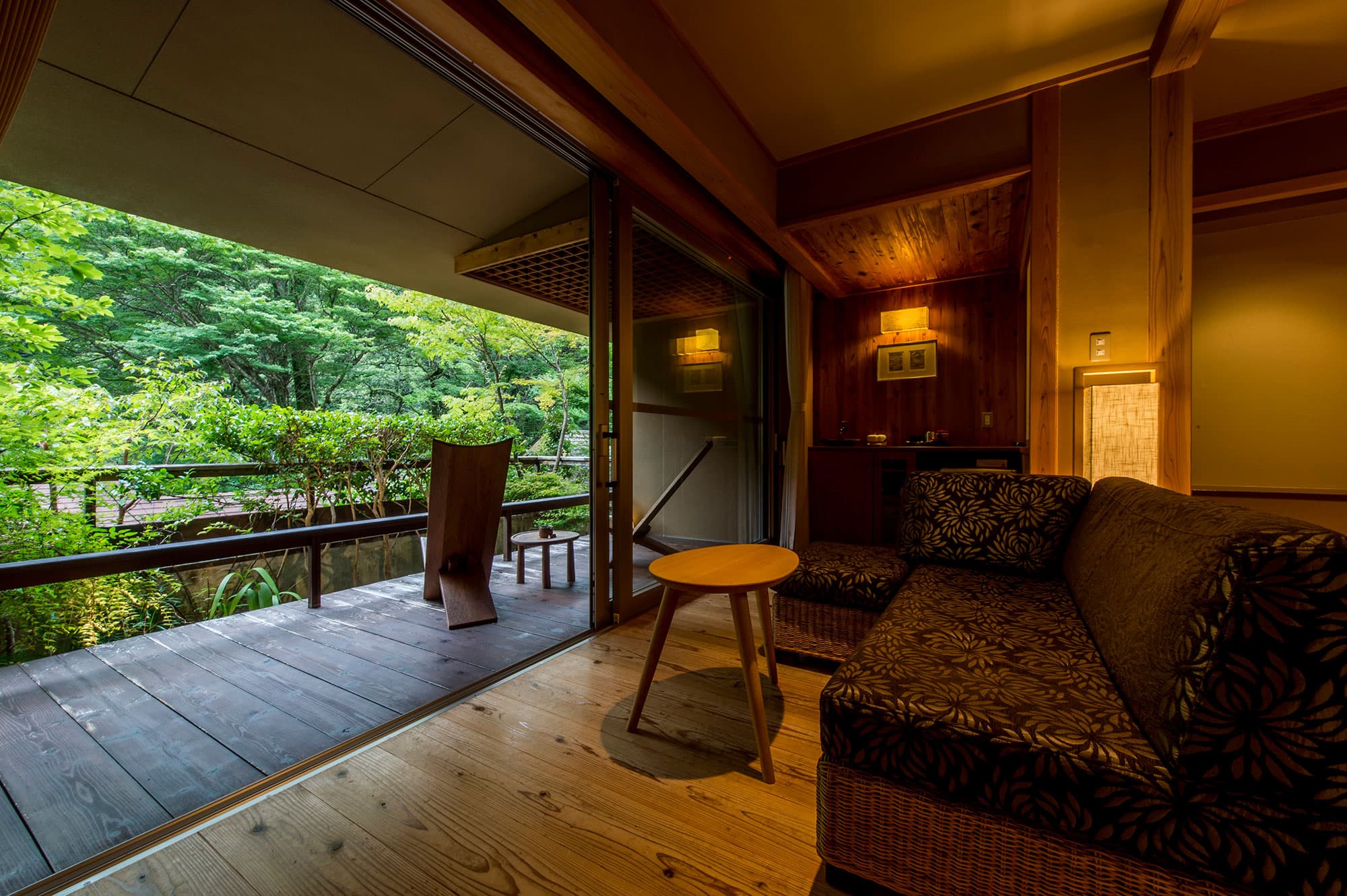 Guest room at Asebino with a patterned sofa and private wooden balcony overlooking the riverside forest, Izu