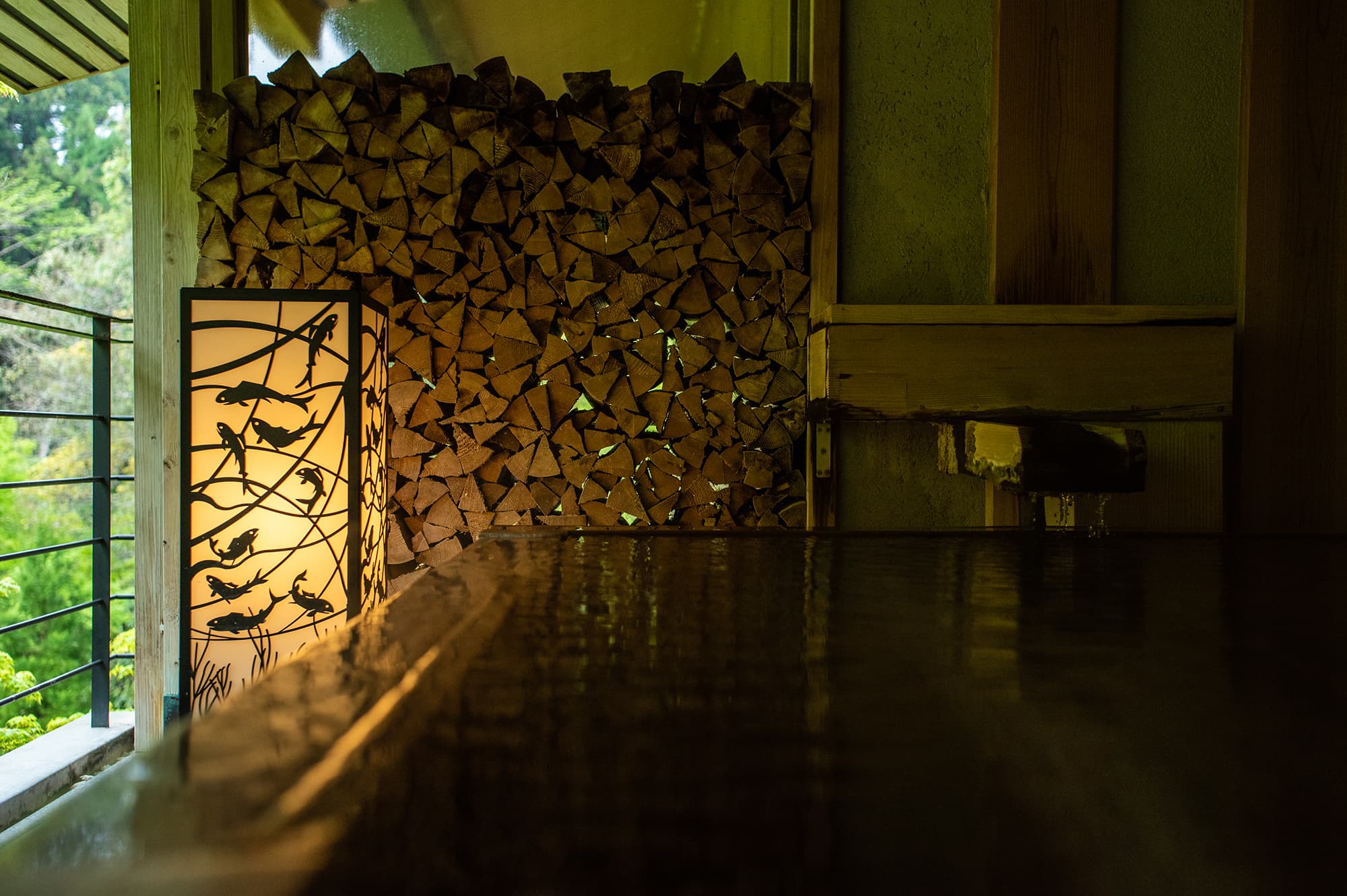 Riverside open-air bath at Asebino with a polished wood deck, stacked-firewood wall and koi-motif lantern, Yugashima Onsen Izu