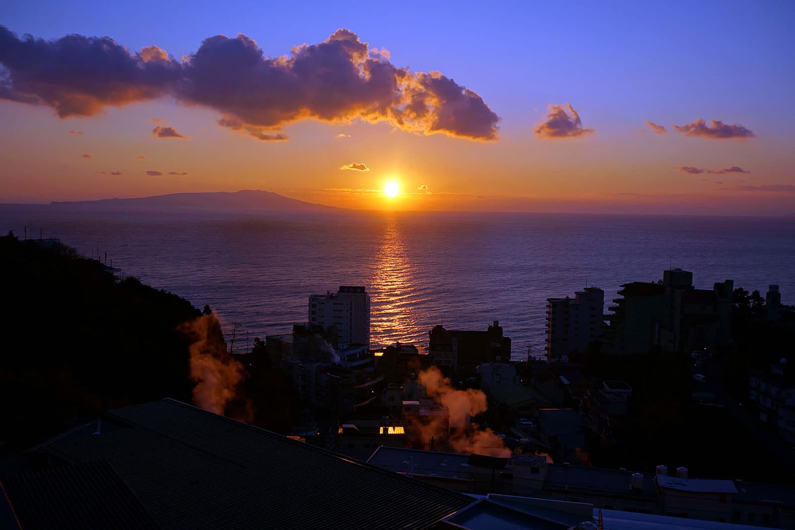 Sunrise over the ocean toward Izu Oshima with onsen steam rising from Atagawa Onsen town below the hotel