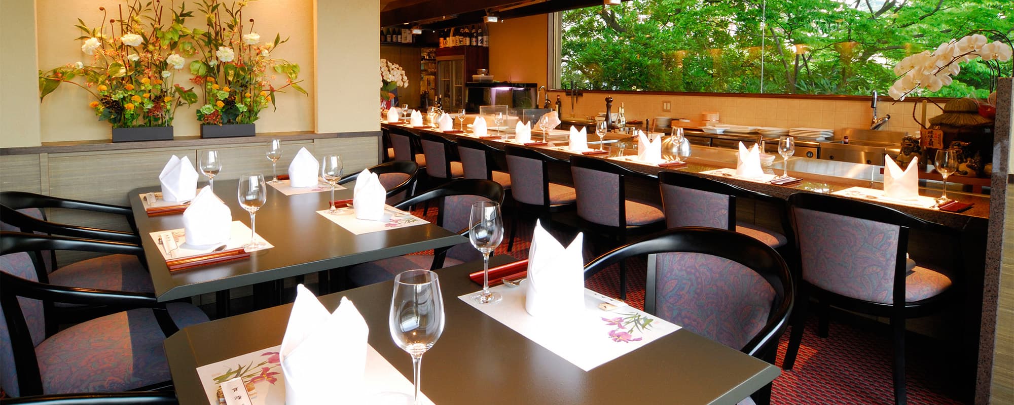 Teppanyaki restaurant with set tables, counter seating and a green garden view at Atami Taikanso