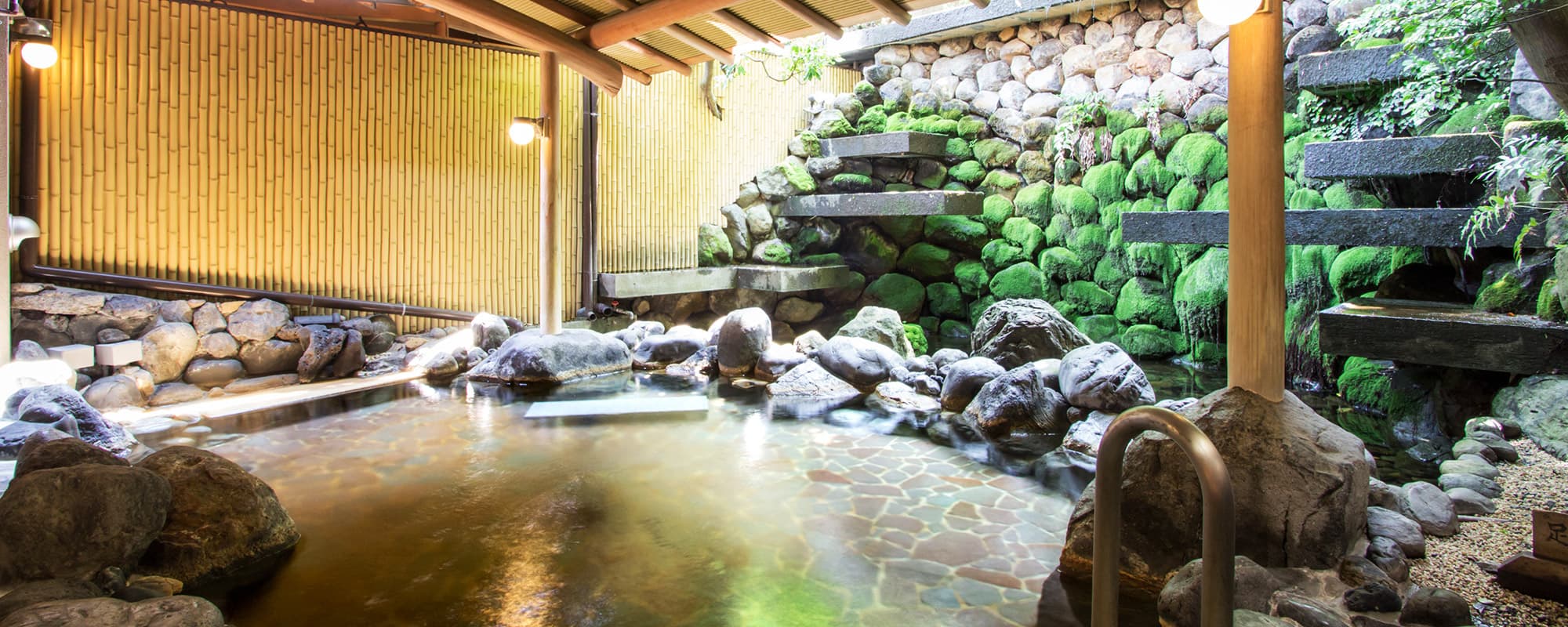 Open-air rotenburo bath surrounded by moss-covered stone walls and a small waterfall at Atami Taikanso