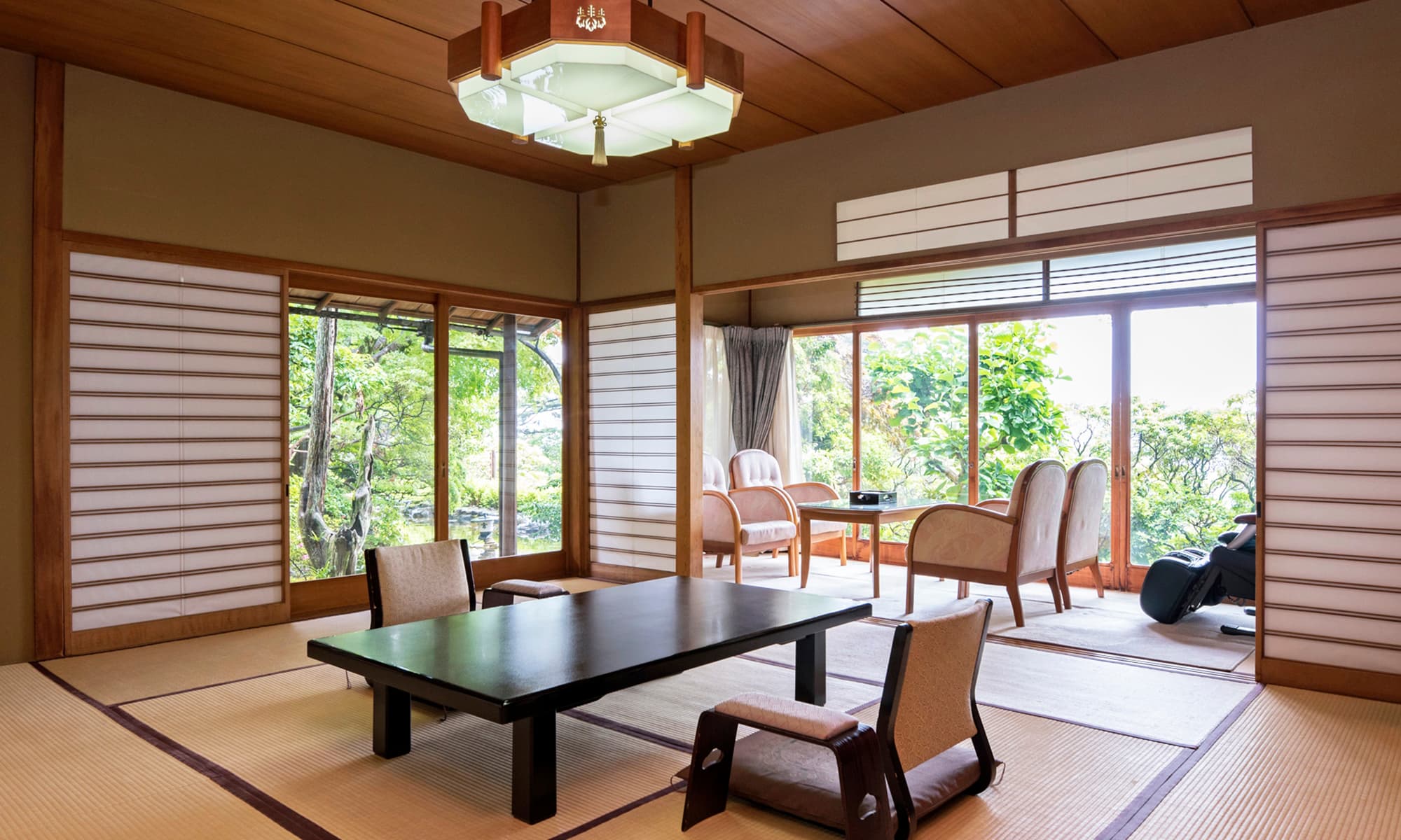 Spacious tatami guest room with low table and floor chairs facing a garden through shoji windows at Atami Taikanso