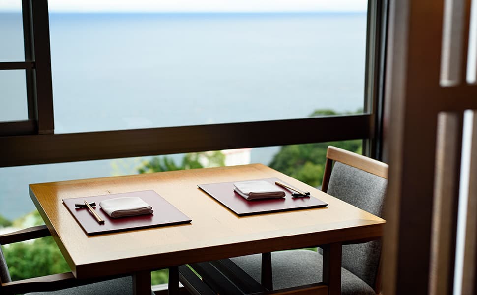 Atami Sekaie dining table set for two with ocean horizon view through floor-to-ceiling windows