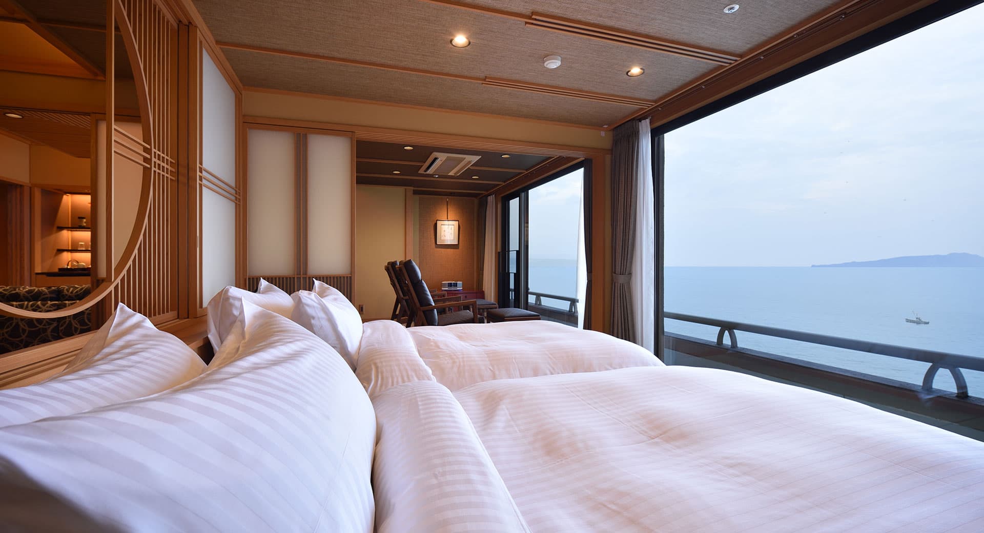 Sixth-floor guest room at Bousui with twin beds, shoji-screen details and a wide ocean view through floor-to-ceiling windows