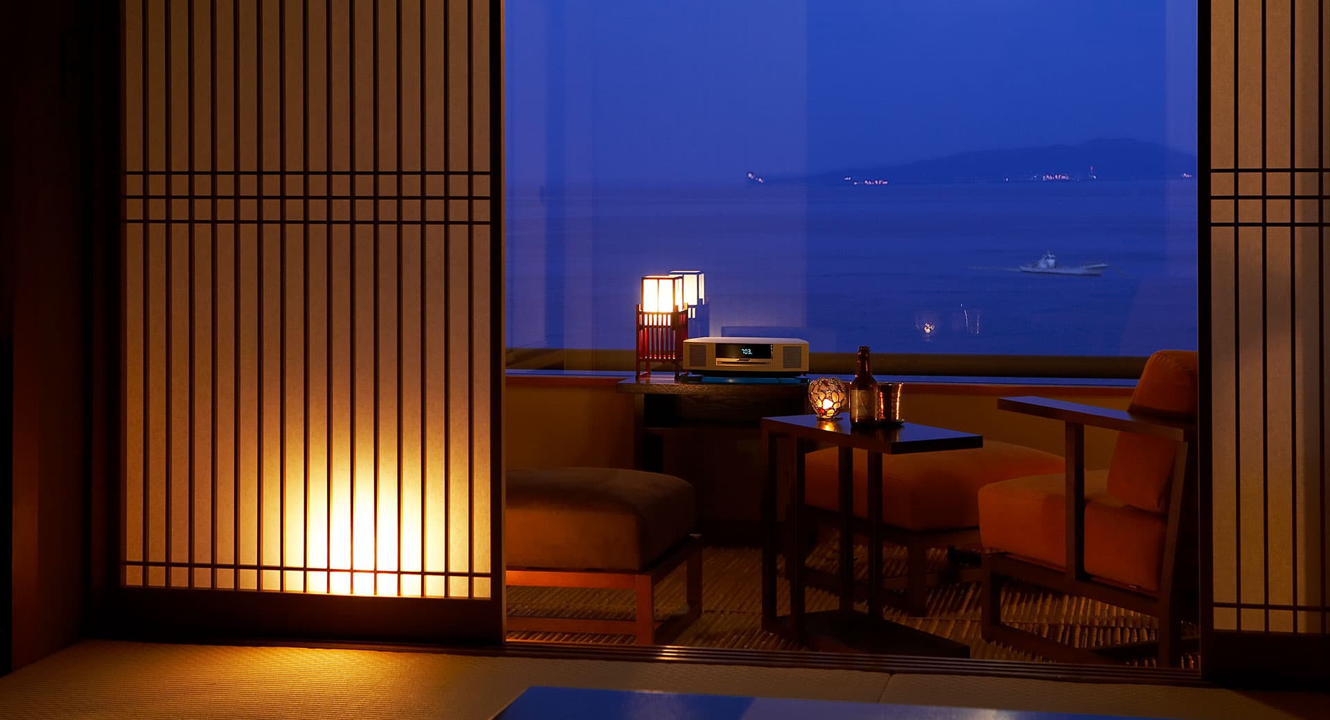 Seventh-floor guest room at Bousui at dusk, with low lounge chairs and a lantern framing the Sagami Bay seascape