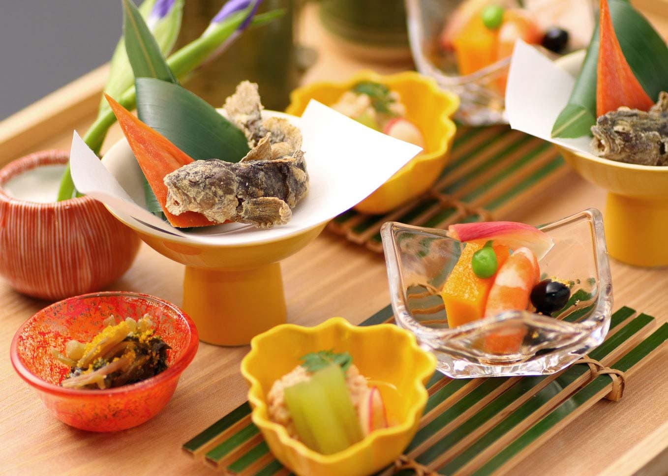 Assorted kaiseki appetizers in colorful Kutani and glass dishes on a bamboo tray at Ryokan Kanazawa Chaya