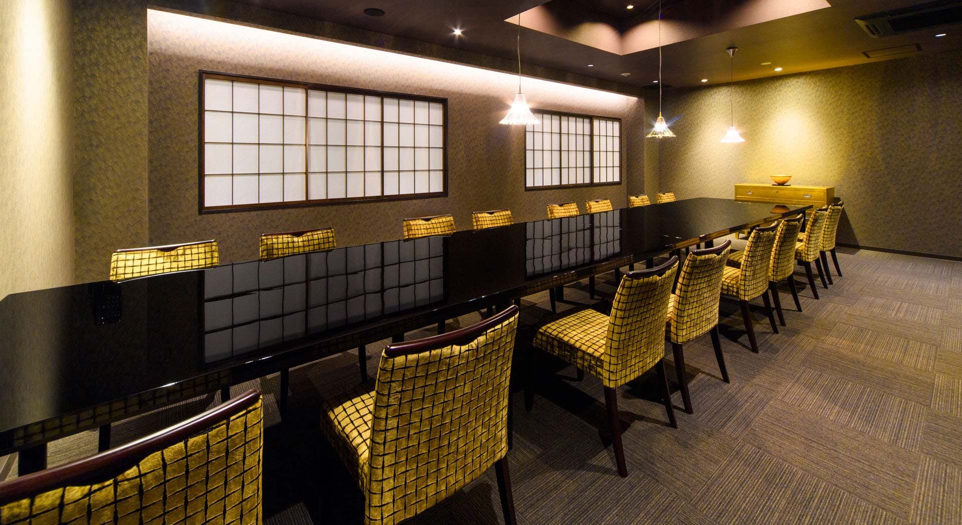 Private dining room with a long black lacquer table, shoji windows and warm lighting at Ryokan Kanazawa Chaya