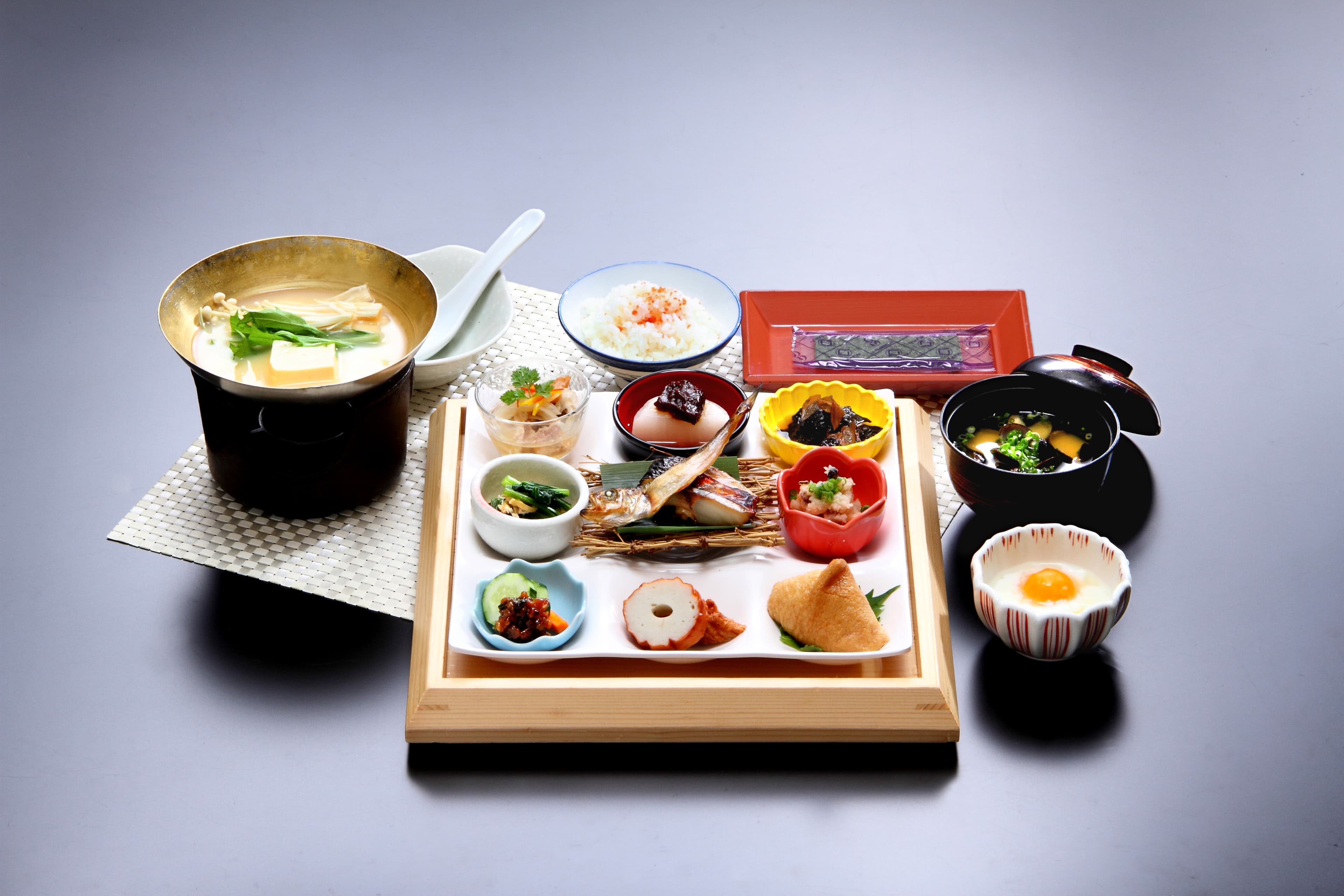 Japanese breakfast set with rice, grilled fish, hot pot and small dishes on a wooden tray at Yujin Chiyonoyu
