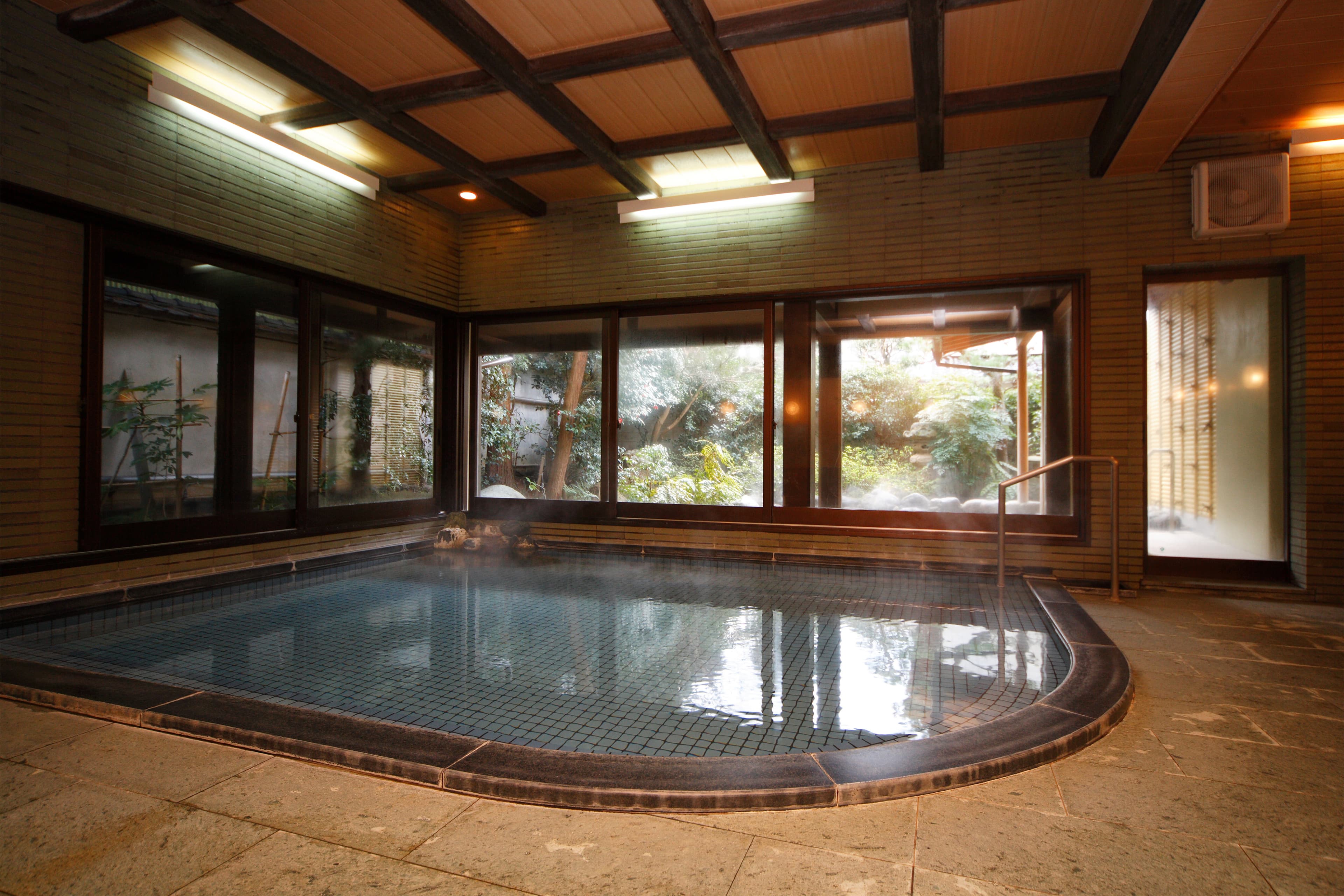 Spacious indoor hot-spring bath with timber-beam ceiling and steam at Yujin Chiyonoyu, Tamatsukuri Onsen