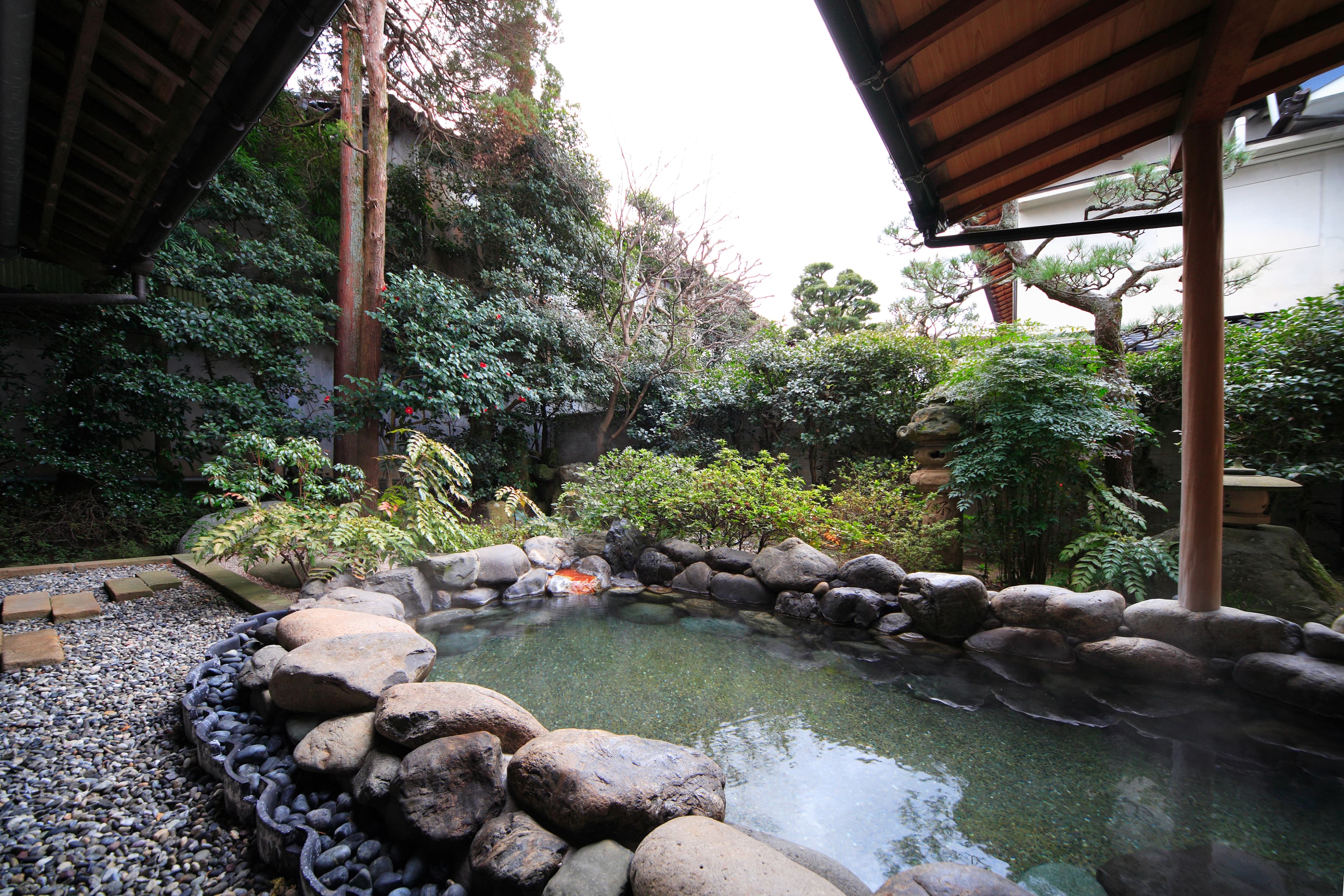 Rock-framed open-air onsen bath with manicured pine garden at Yujin Chiyonoyu, Tamatsukuri Onsen