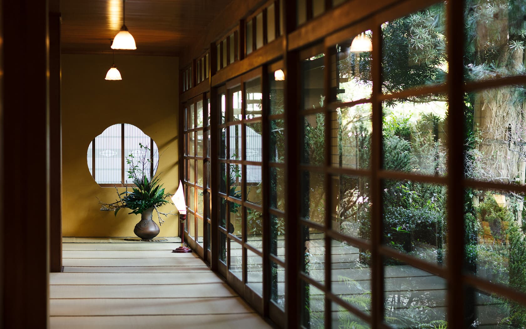 Interior corridor at Daimaru Besso with a round window, ikebana arrangement and glass walls opening onto the garden