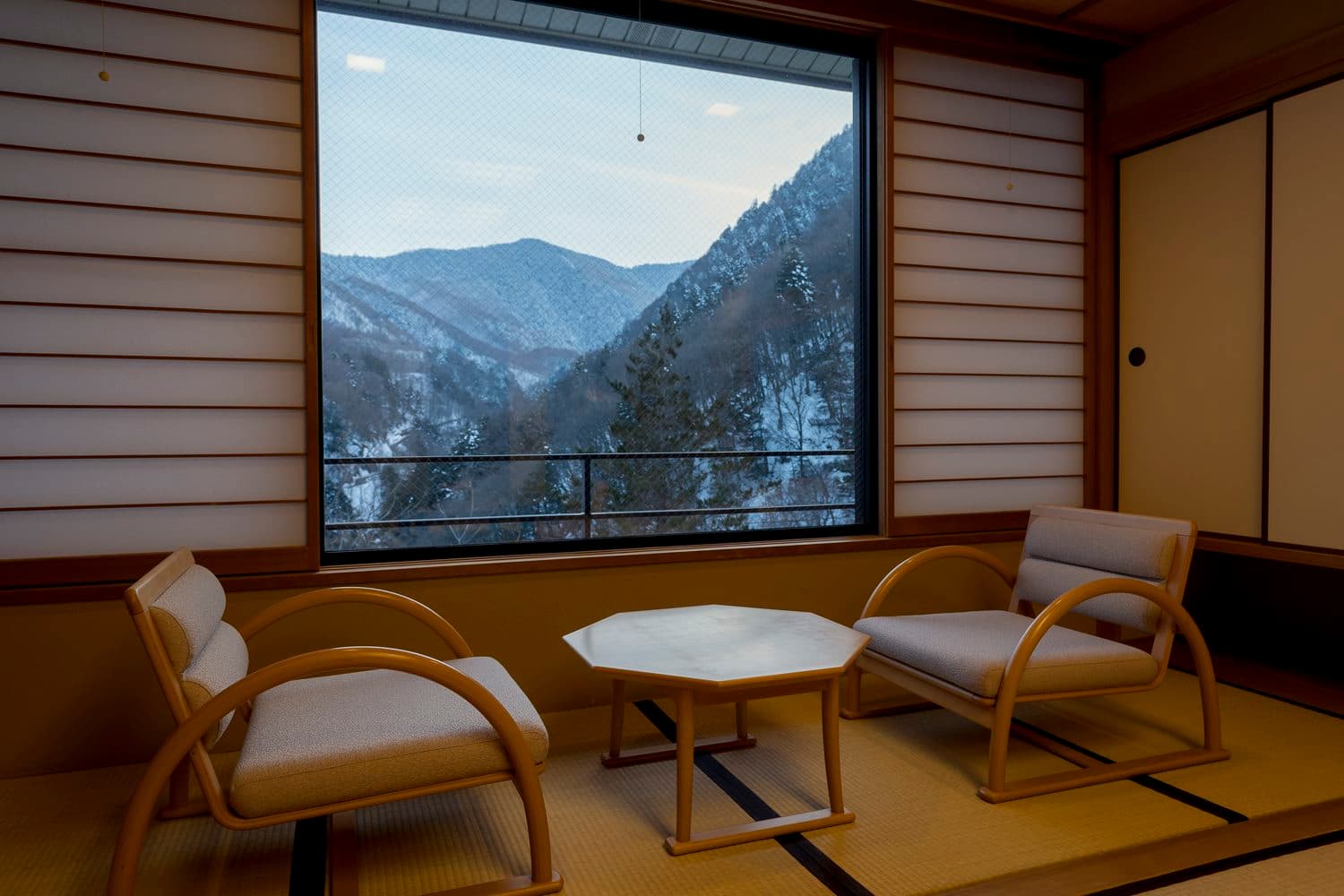 Tatami room with wicker chairs framing a window over snow-dusted mountains at Shirahone Ebisuya