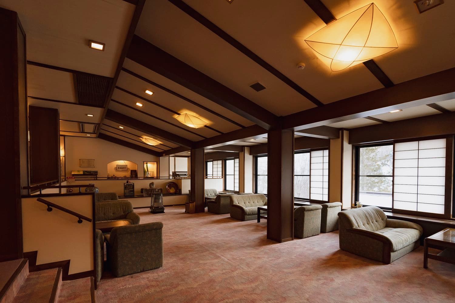 Warmly lit lounge with sofas, exposed beams and shoji windows at Shirahone Ebisuya