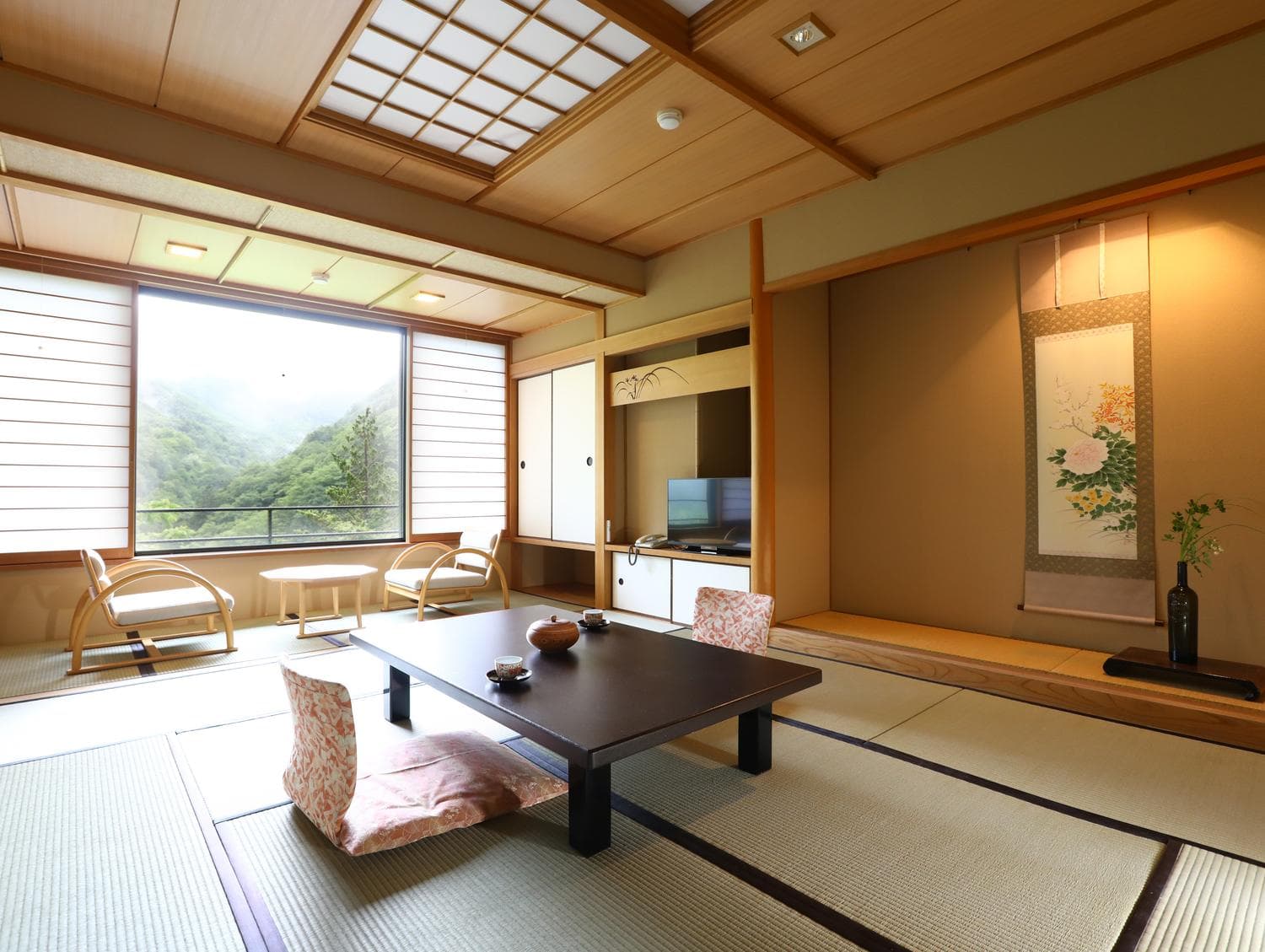 Spacious tatami guest room with low table, hanging scroll and valley view at Shirahone Ebisuya
